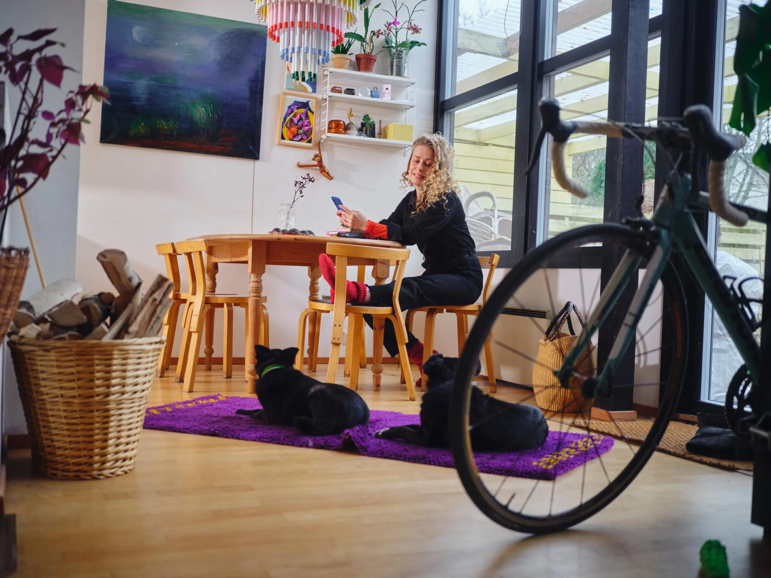 Ida Tamminen istuu keittön pöydän ääressä ja katsoo lattialla makaavaa mustaa koiraa.