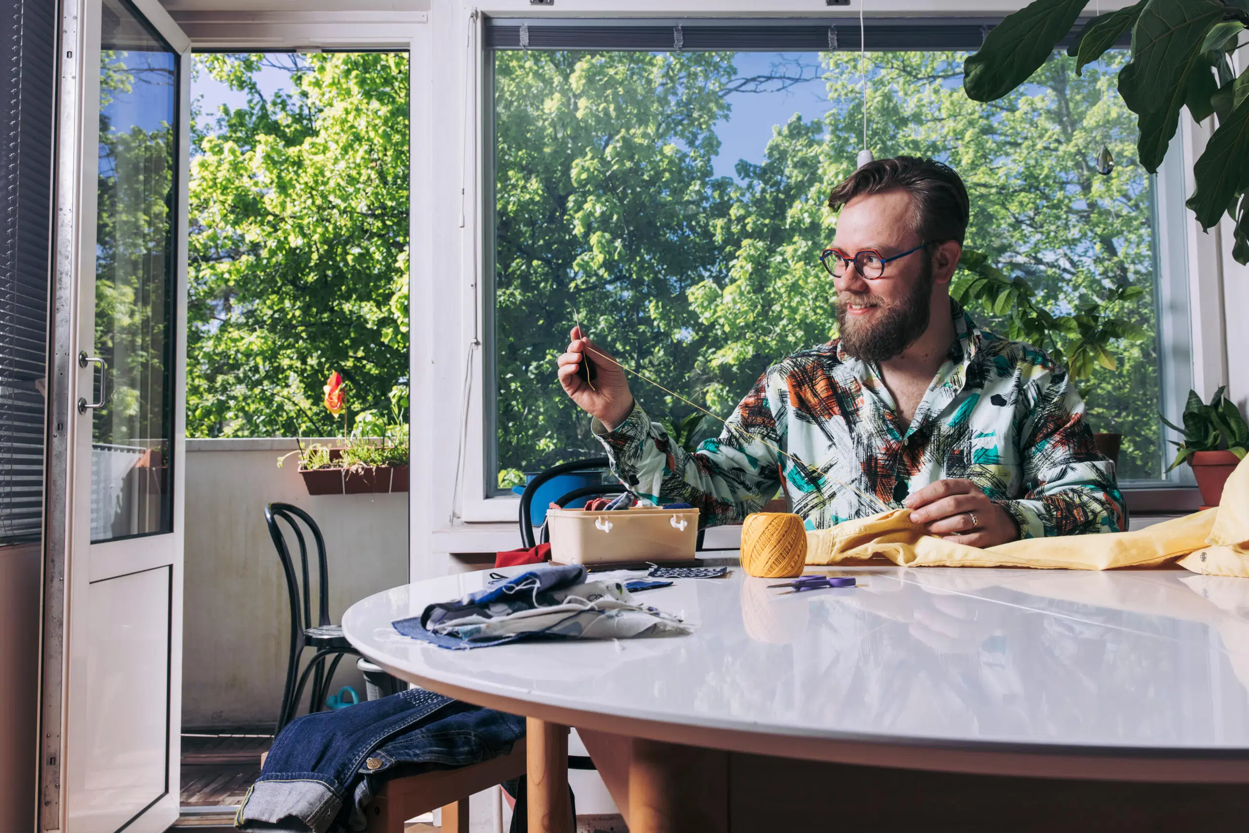 Niko Lindgren ompelee pöydän ääressä, ikkuna auki kohti vihreää pihaa.