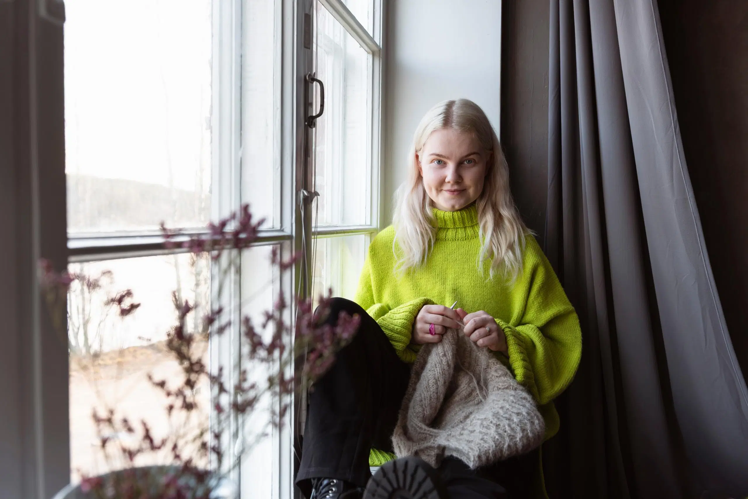 Elsi Vankka istuu ikkunalaudalla neulomassa.