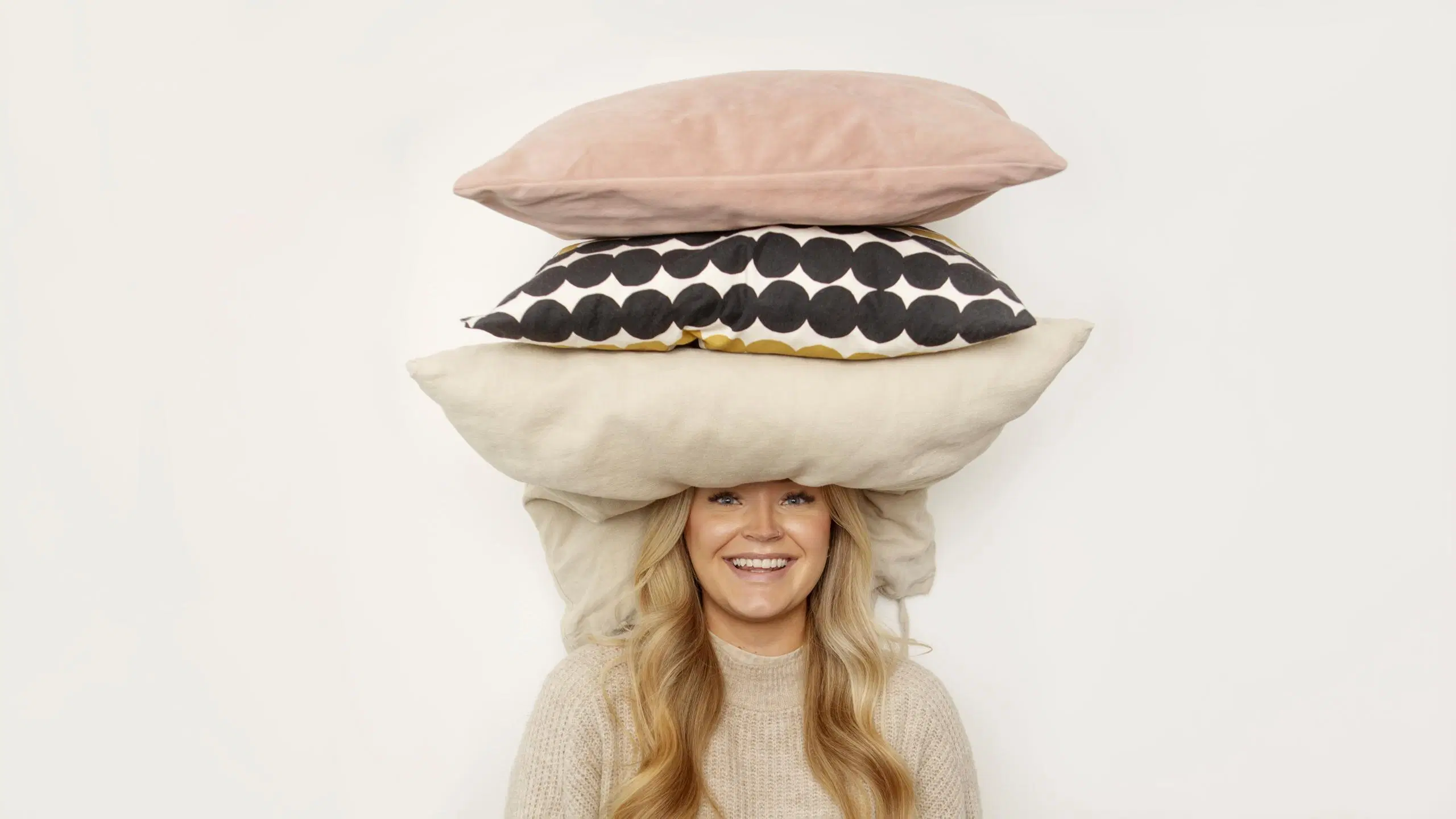 Emilia Tukiainen nauraa kohti kameraa, pään päälle kasattu kolme tyynyä