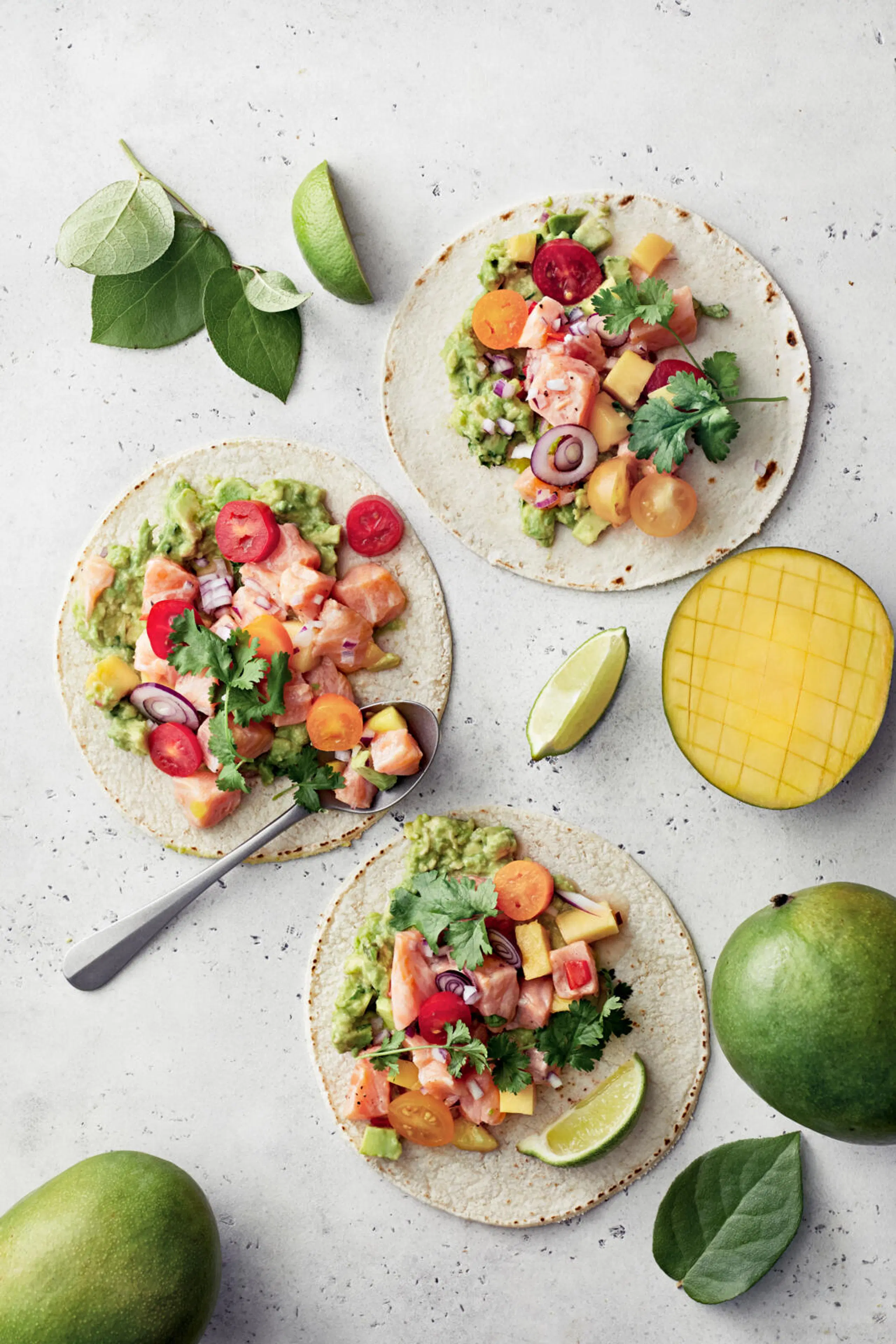 Kolme tacoa täytettynä mango-lohicevichellä. Ympärillä limeviipaleita ja mangoja.