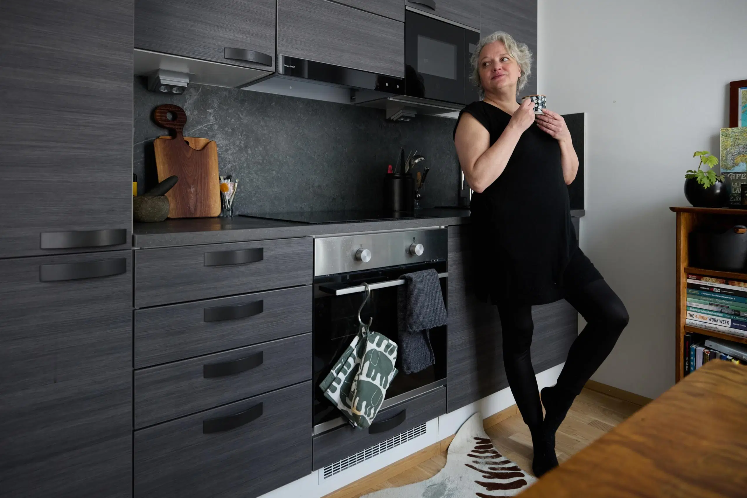 Tanja Mikkola seisoo keittiössä, nojaa keittiön kaappeihin.