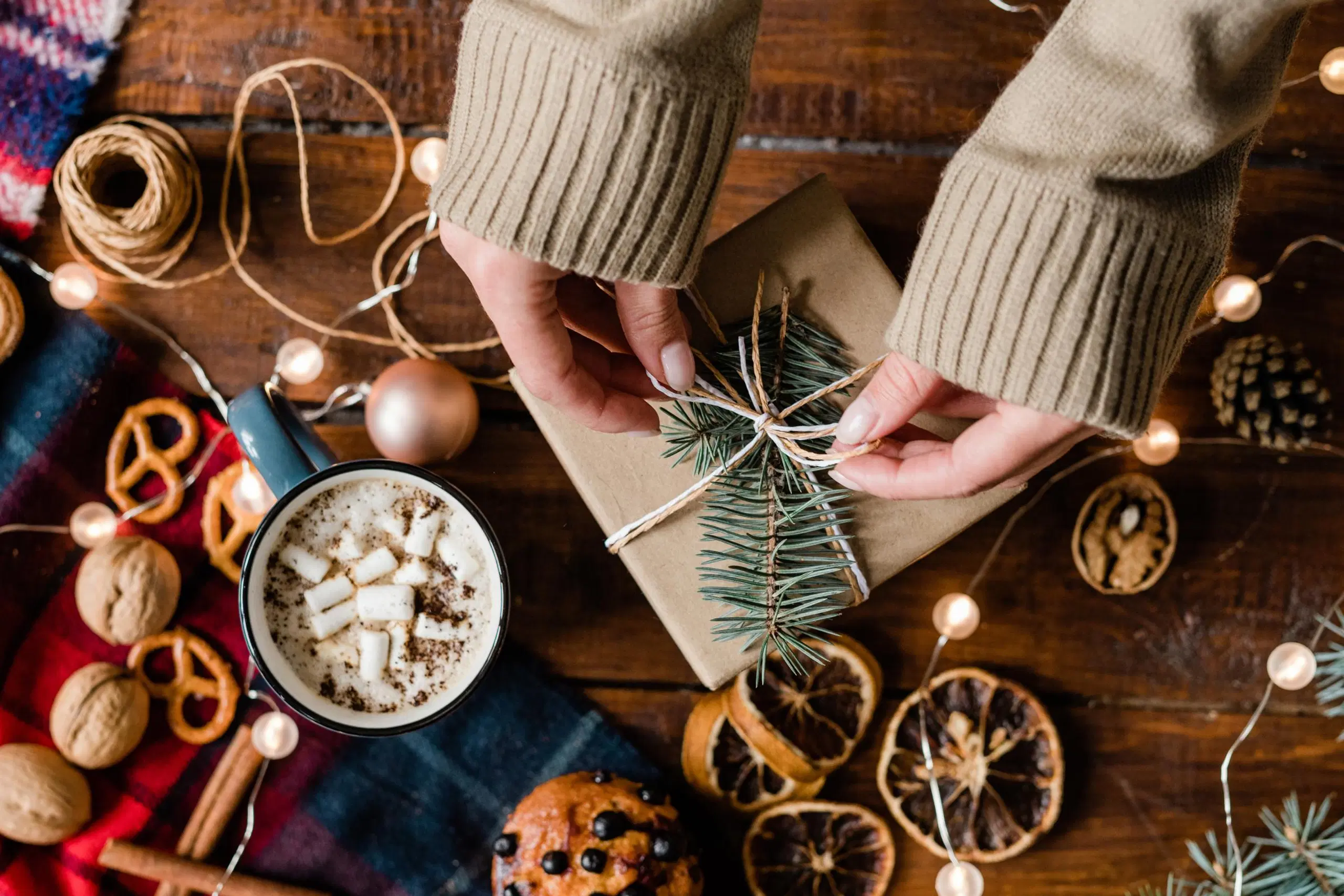 Itse tehtyn lahjan paketointi, ympärillä kuivattuja appelsiineja, jouluvalot ja herkkuja