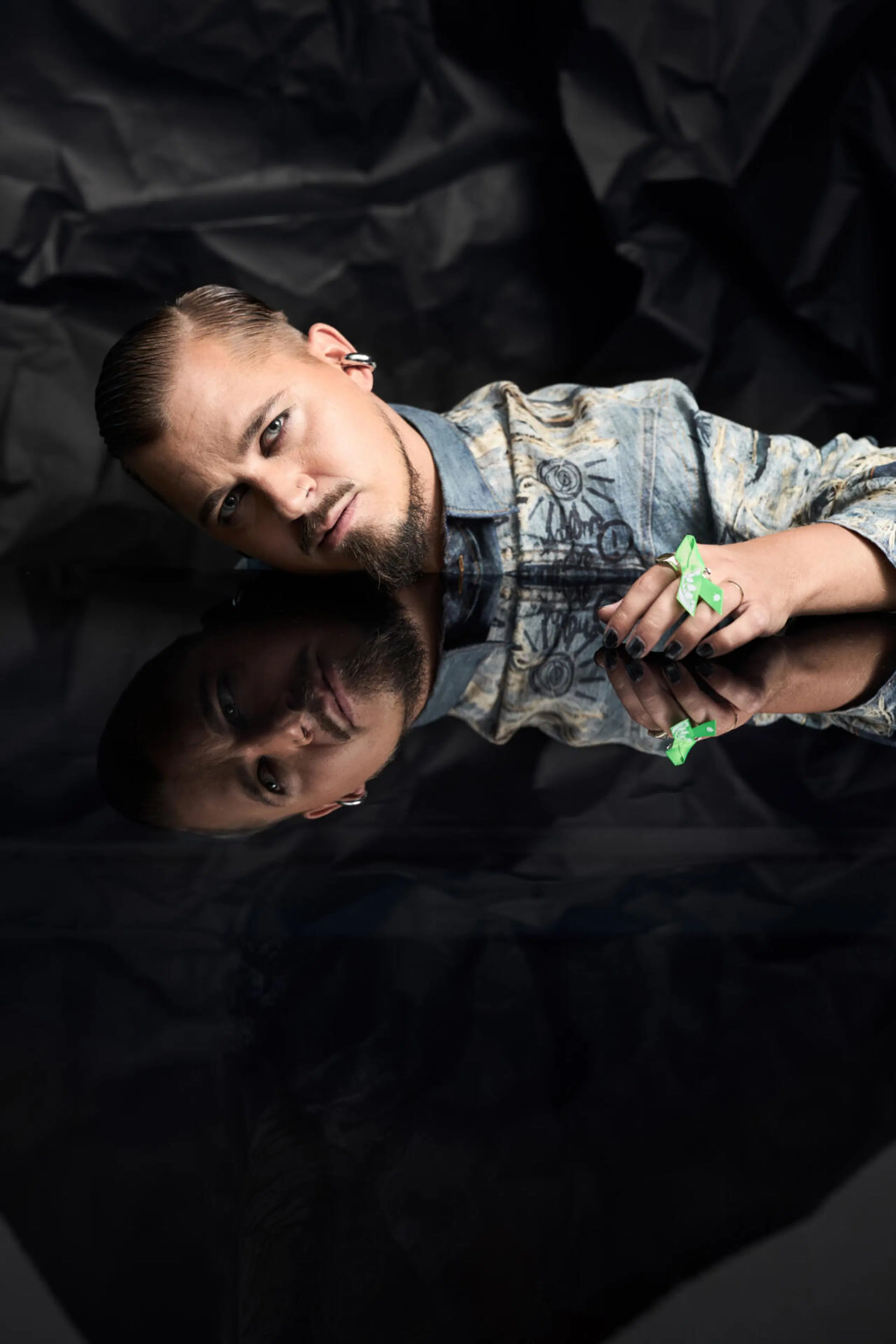 Jere Pöyhönen nojaa peilaavaa mustaa pöytää vasten Mielinauha kädessään ja katsoo kameraan.