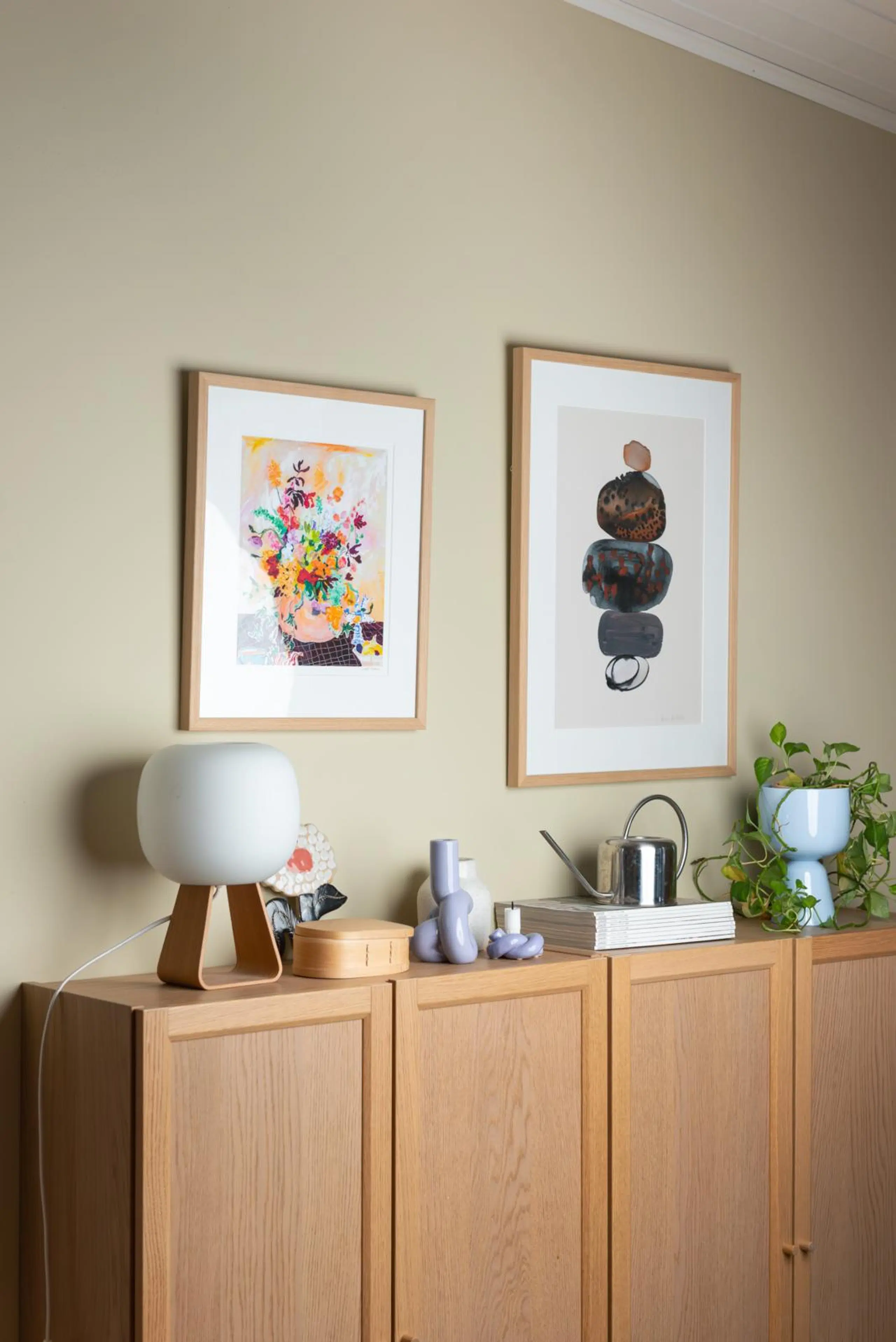 Puinen senkki, jonka päällä on koriste-esineitä ja kasvi. Seinällä senkin yläpuolella on kaksi taulua.