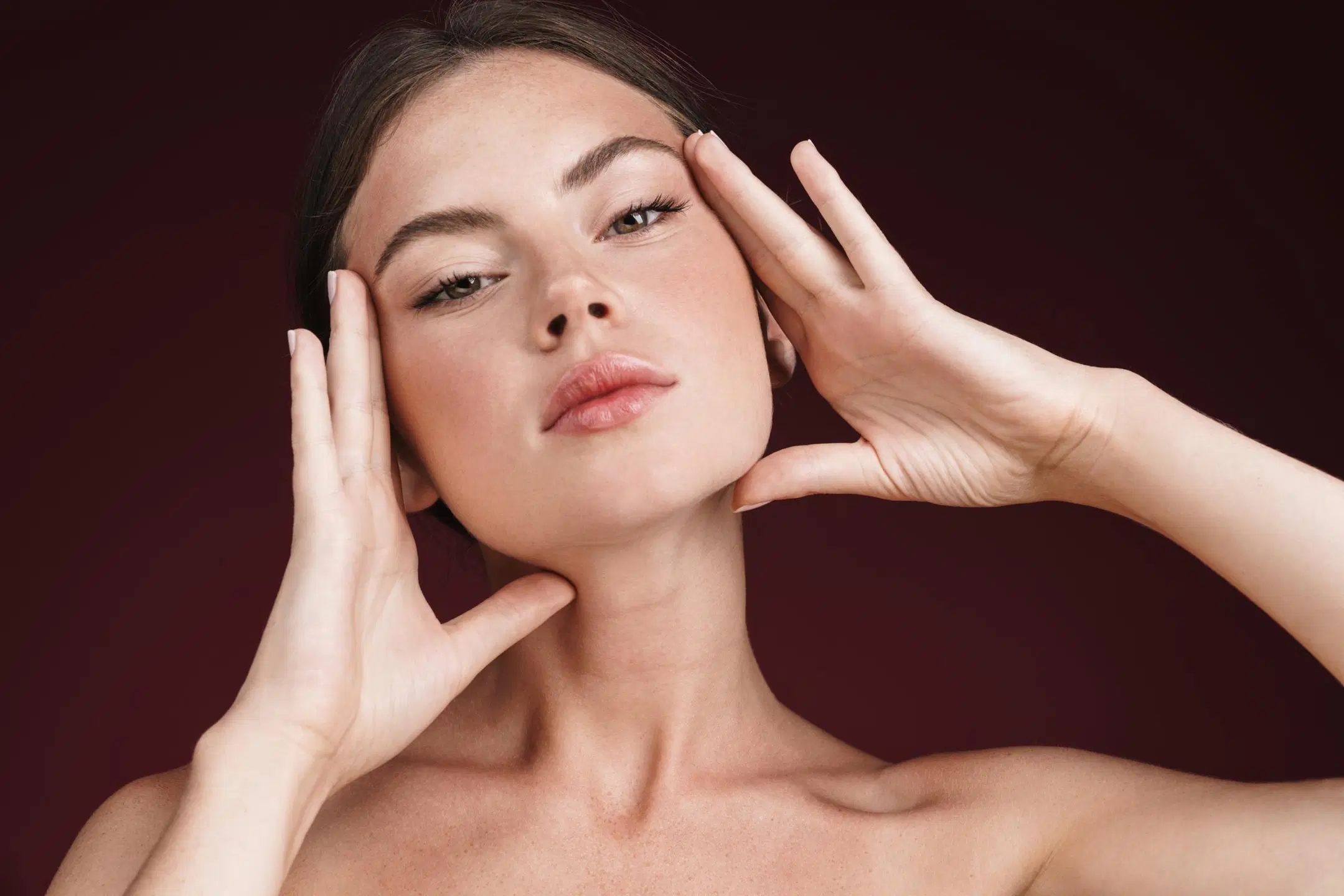 Nainen kehystää käsillä kasvojaan ja katsoo suoraan kameraan