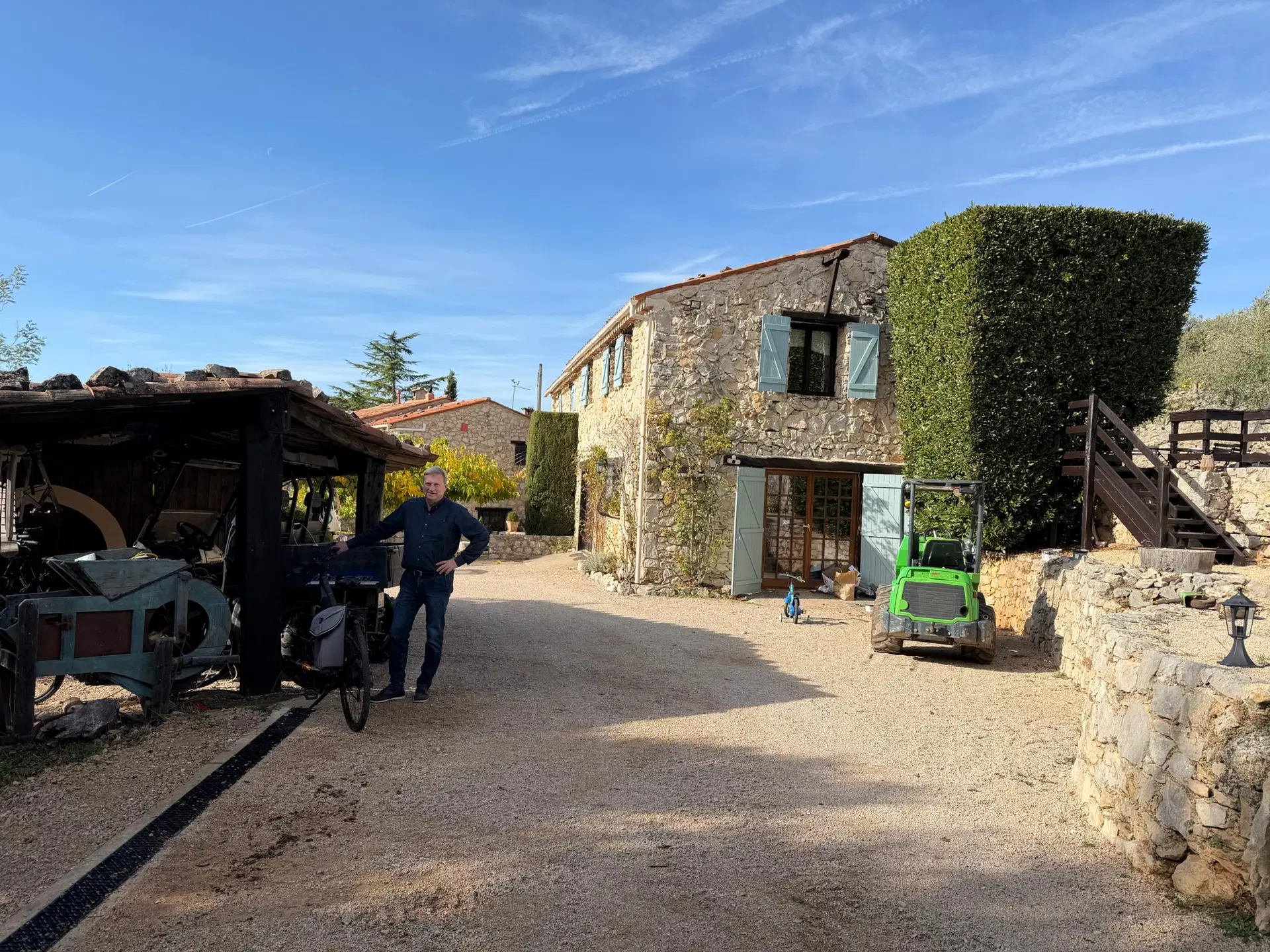 Mies seisoo ränsistyneen talon edessä traktorin vieressä