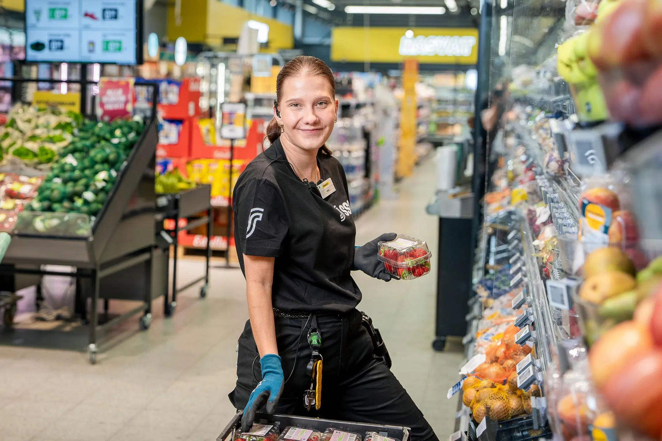 Kaupan myyjä, nuori nainen polvillaan vihanneshyllyn edessä. 