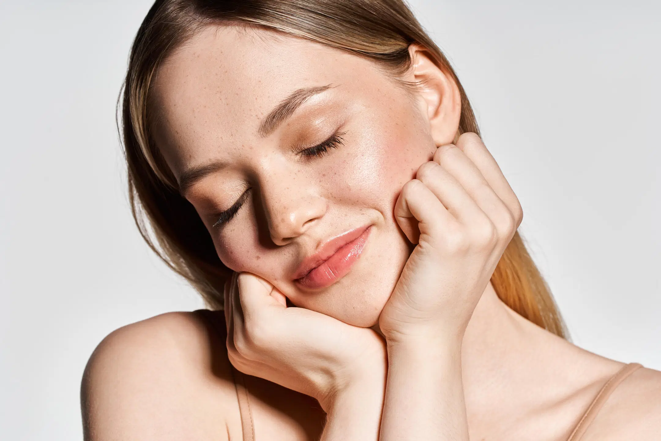 Vaalea, luonnollisesti meikattu nainen poseeraa silmät kiinni ja nojaa käsiinsä