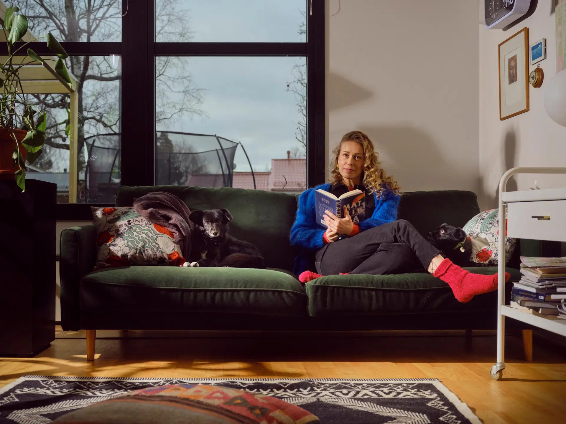 Ida Tamminen istuu olohuoneen sohvalla kirja kädessä koira vierellään.