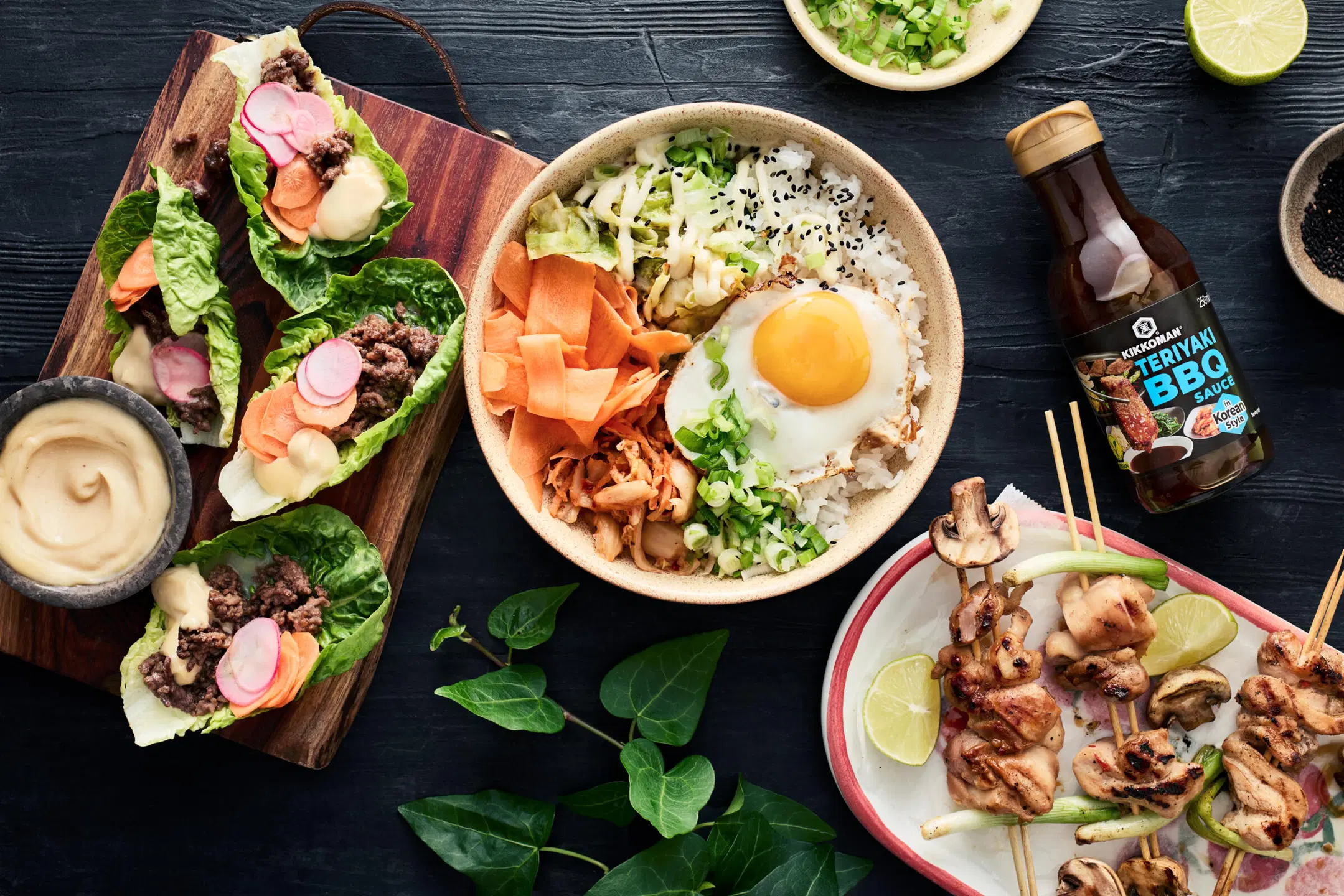 Tummalla alustalla bibimbap varhaiskaalista, salaattitacot ja teriyakimajoneesi ja grillatut kana-herkkusienivartaat ja jogurtti-inkiväärikastike, vaakakuva.