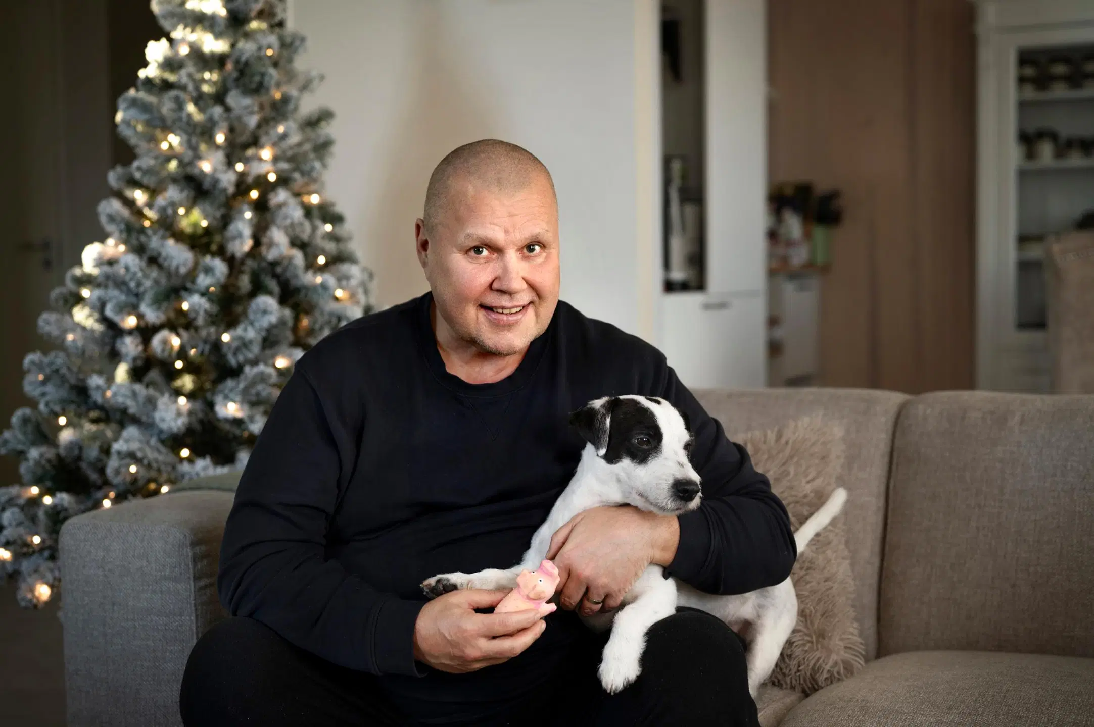 Timo Jutila sohvalla koiransa kanssa. Taustalla joulukuusi.