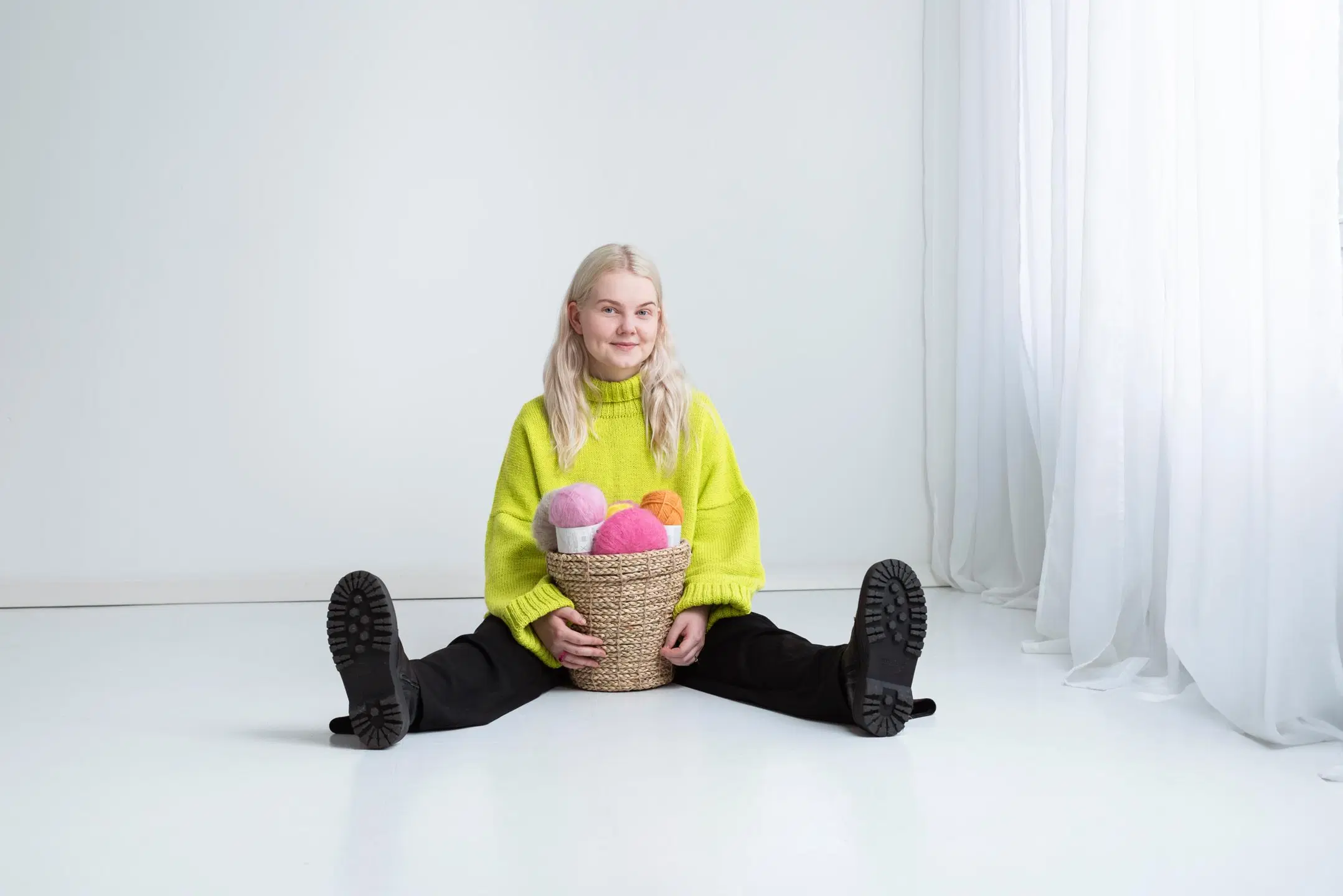 Elsi Vankka istuu lattialla. Hänellä on päällään värikäs neule ja käsissä lankakori.