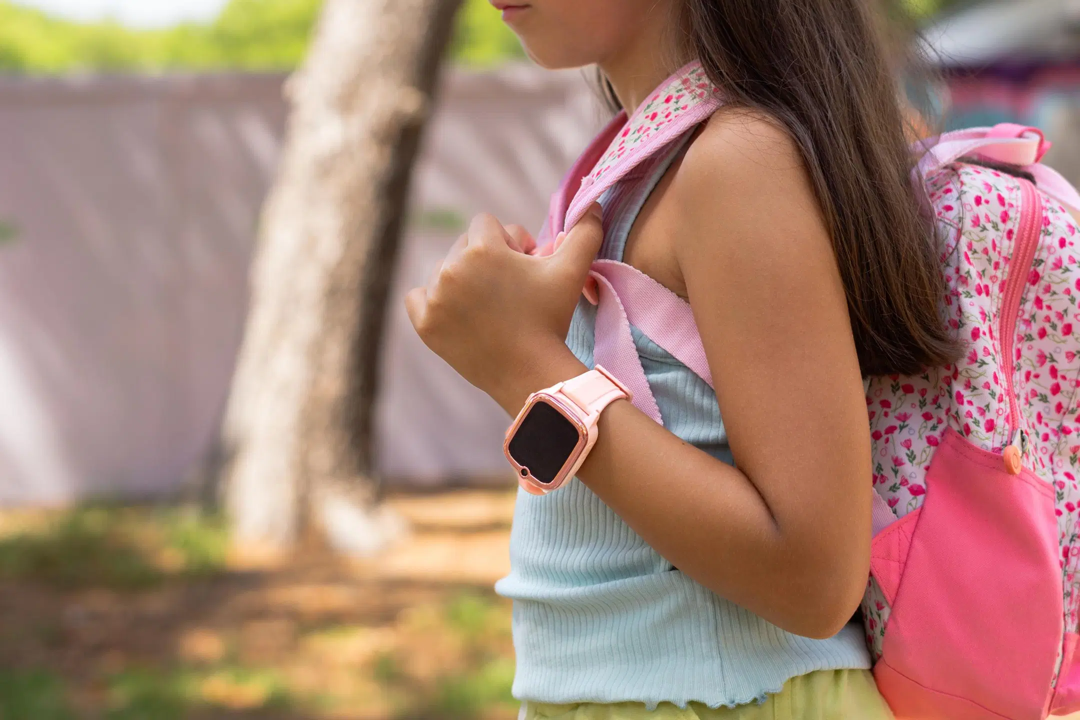 Kouluikäinen lapsi, jolla on ranteessa vaaleanpunainen kellopuhelin ja selässä reppu.