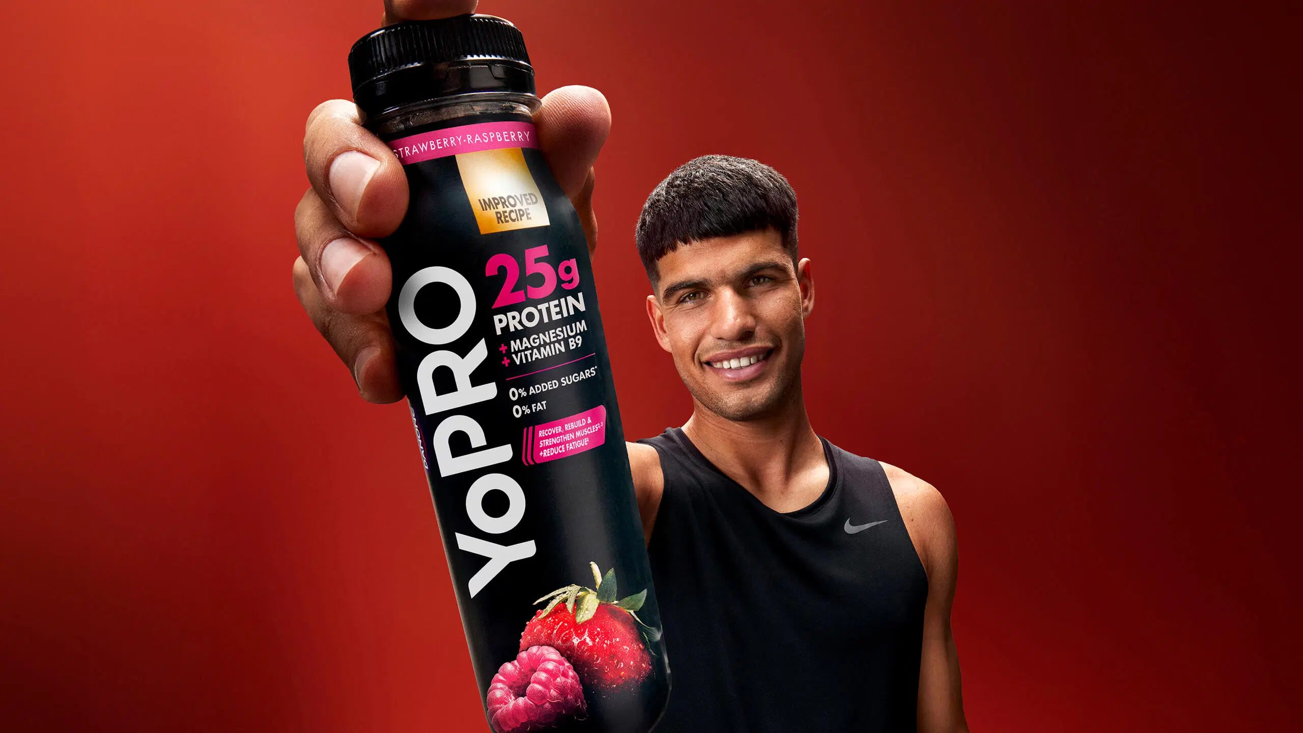 Carlos Alcaraz pitelee kädessään Danone YoPRO -juomaa maussa mansikka-vadelma, punainen tausta