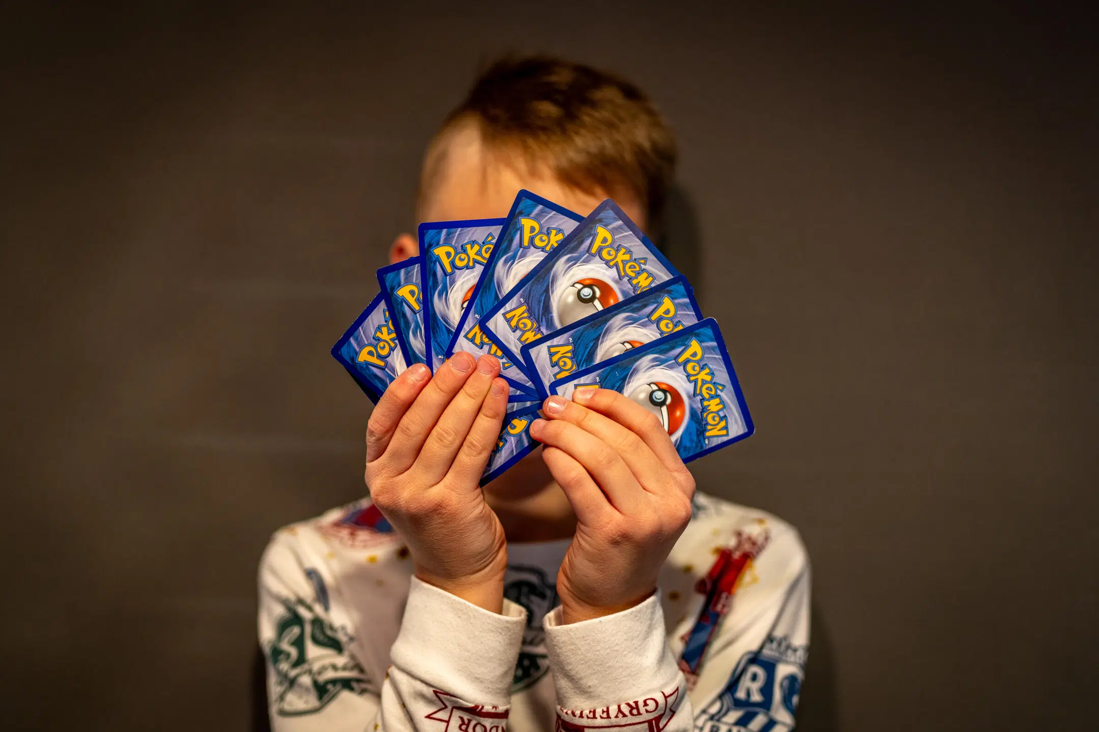 Lapsi pitelee käsissään Pokemon-kortteja ja peittää korteilla kasvonsa