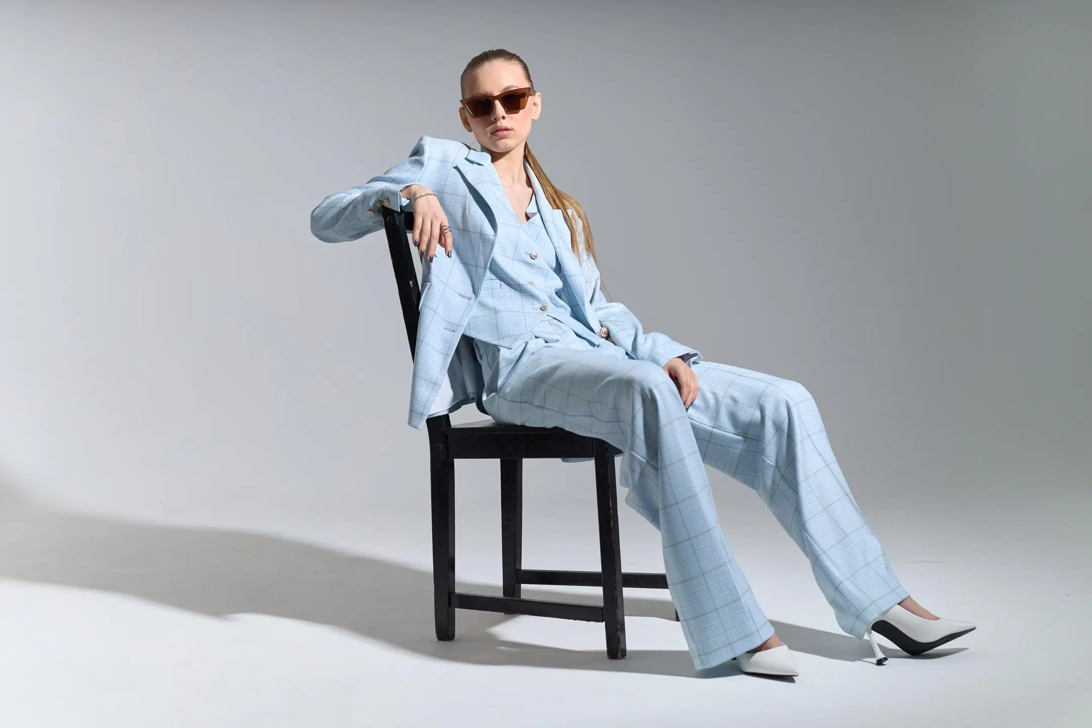 Vaaleansiniseen housupukuun pukeutunut nainen istuu tuolilla rennosti aurinkolasit päässään