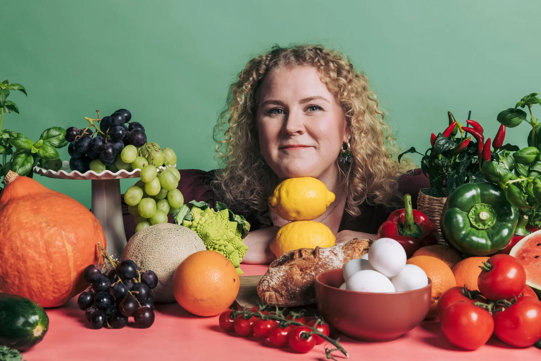 Sonja Kallio, jonka edessä pöytä täynnä värikkäitä kasviksia ja hedelmiä.