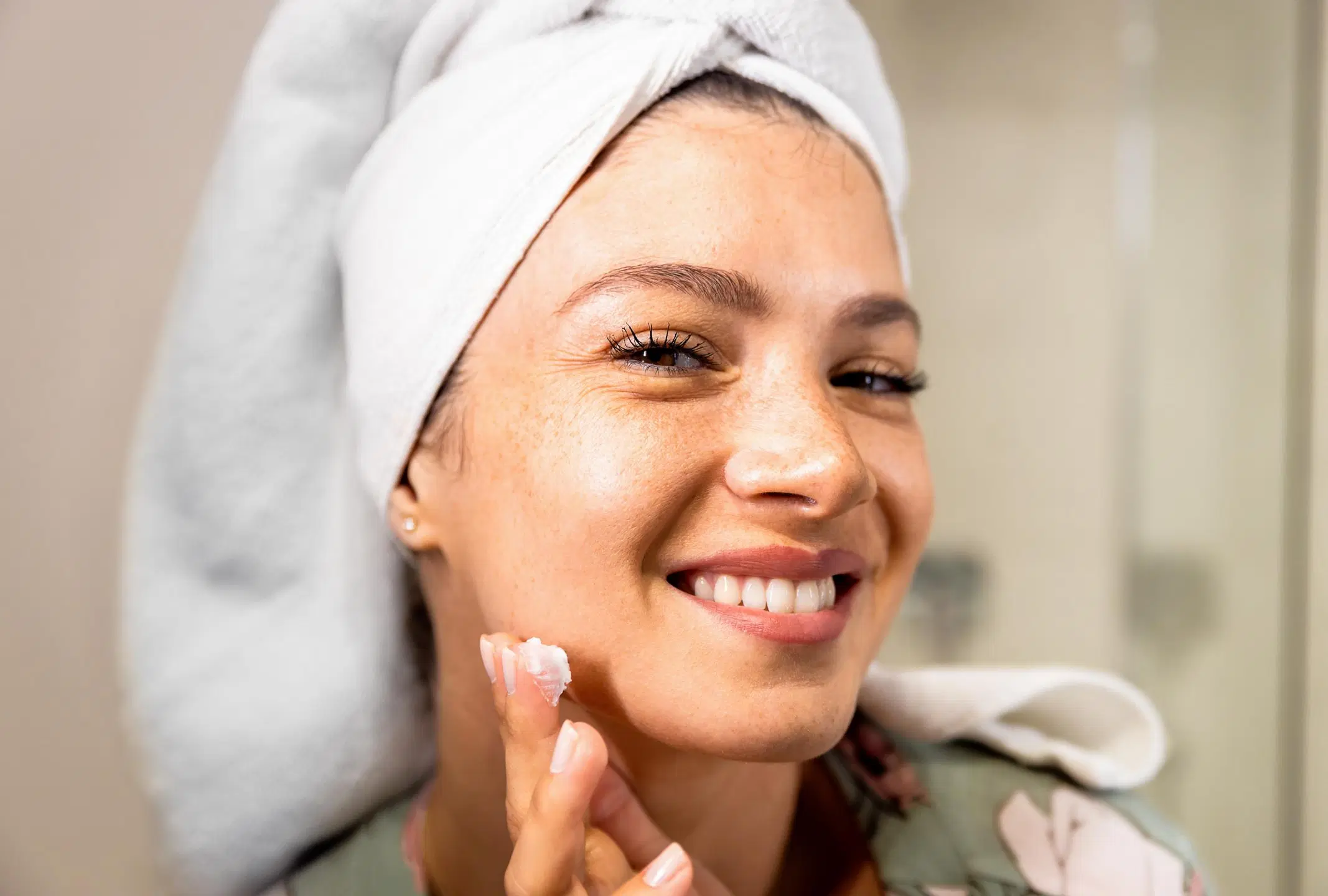 Nainen, jolla on pyyhe päässä, levittää voidetta kasvoilleen