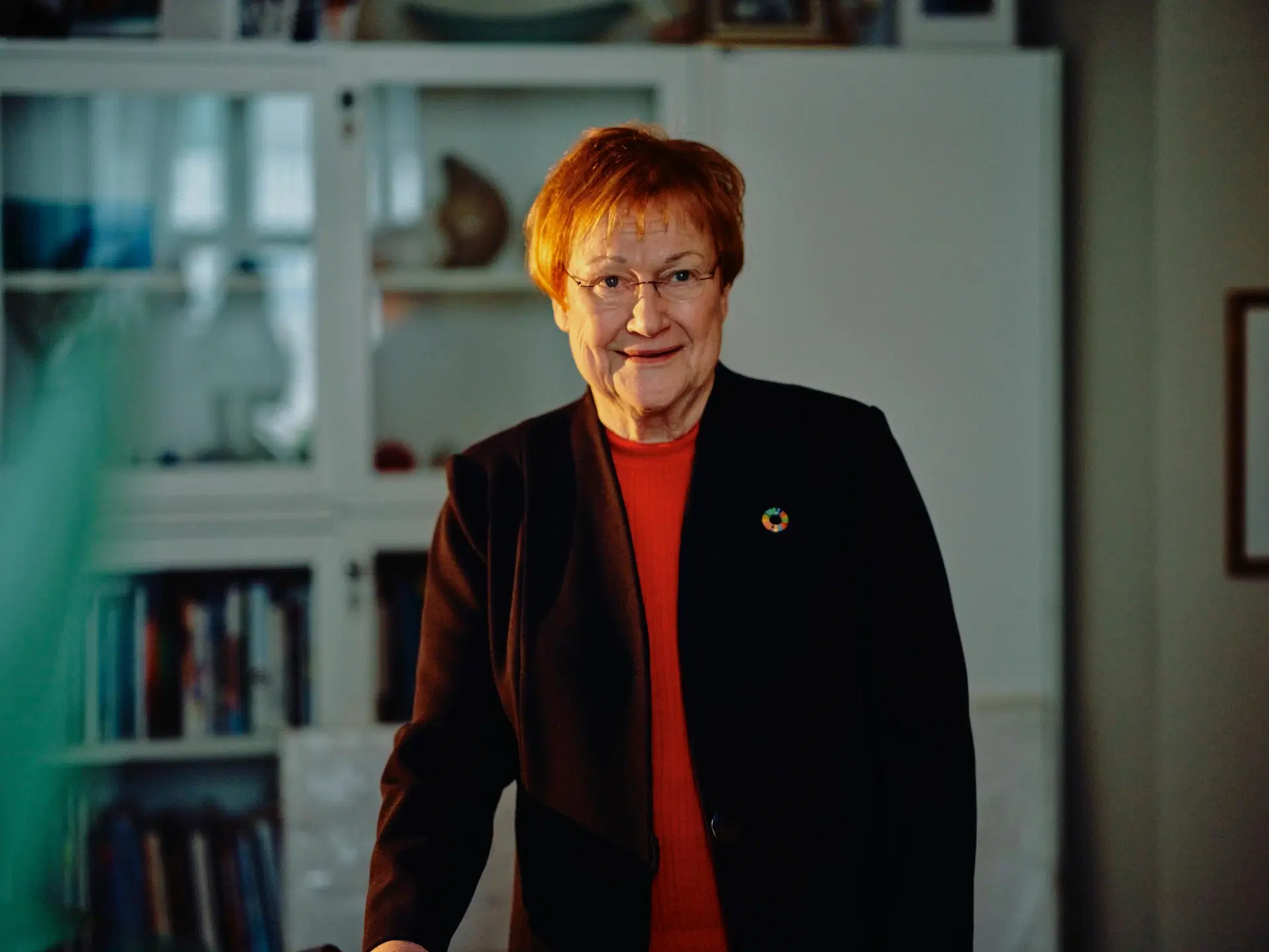 Tarja Halonen seisoo valkoisen vitriinikaapin edessä.