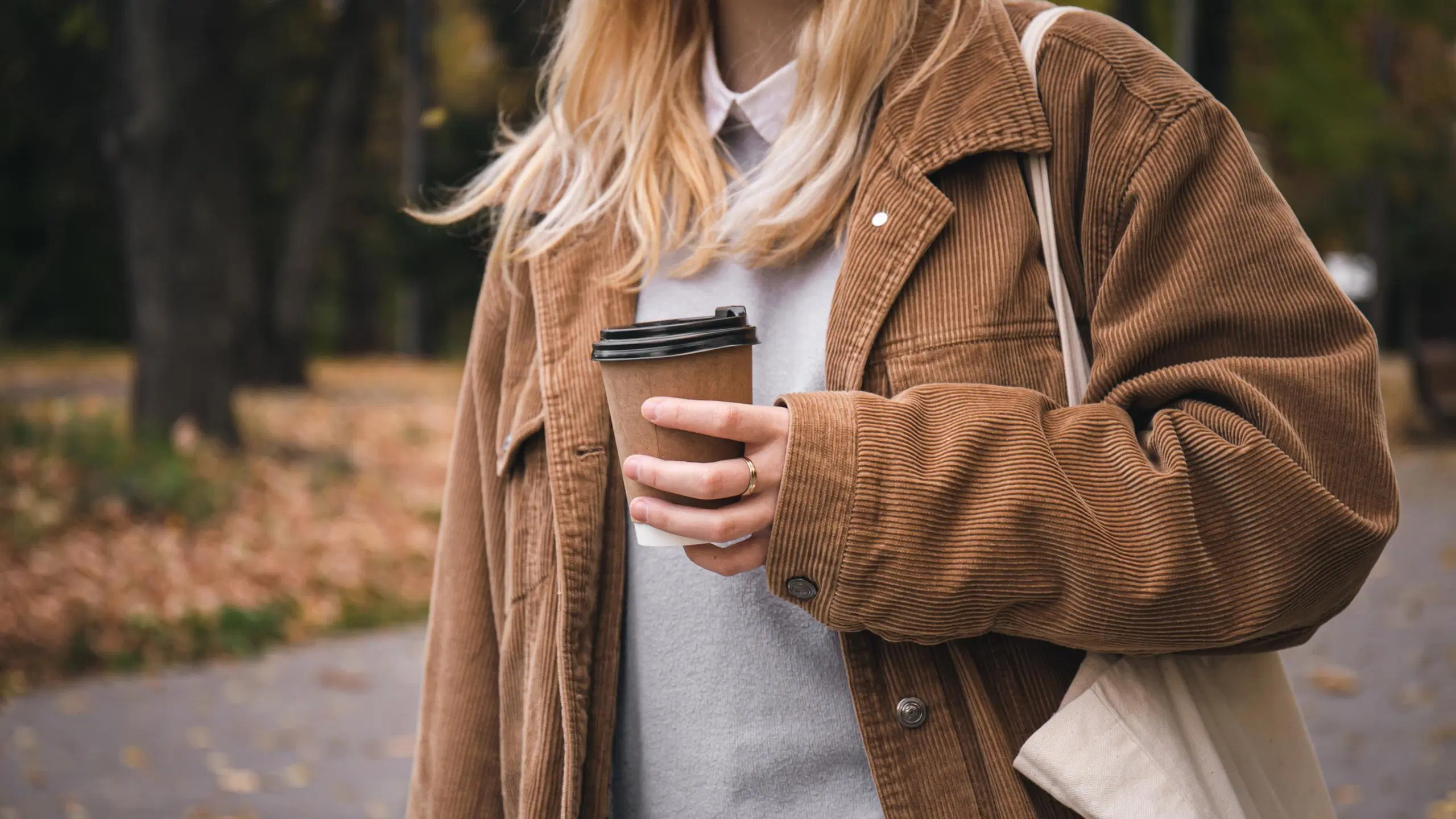 Vaaleaan vakosamettitakkiin pukeutunut nainen, jolla on kädessä take-away-kuppi