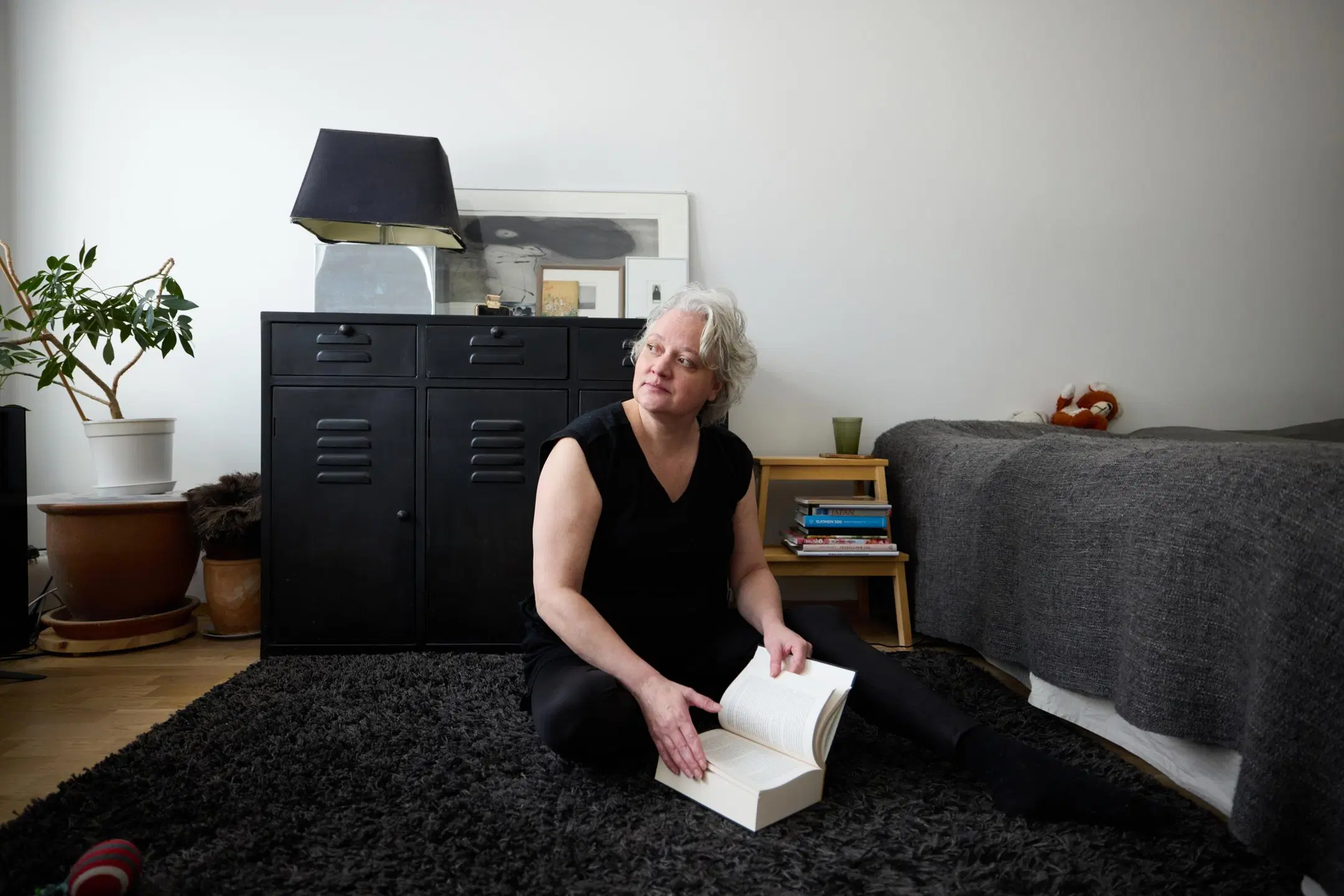 Tanja Mattila istuu lattialla, kädessä kirja