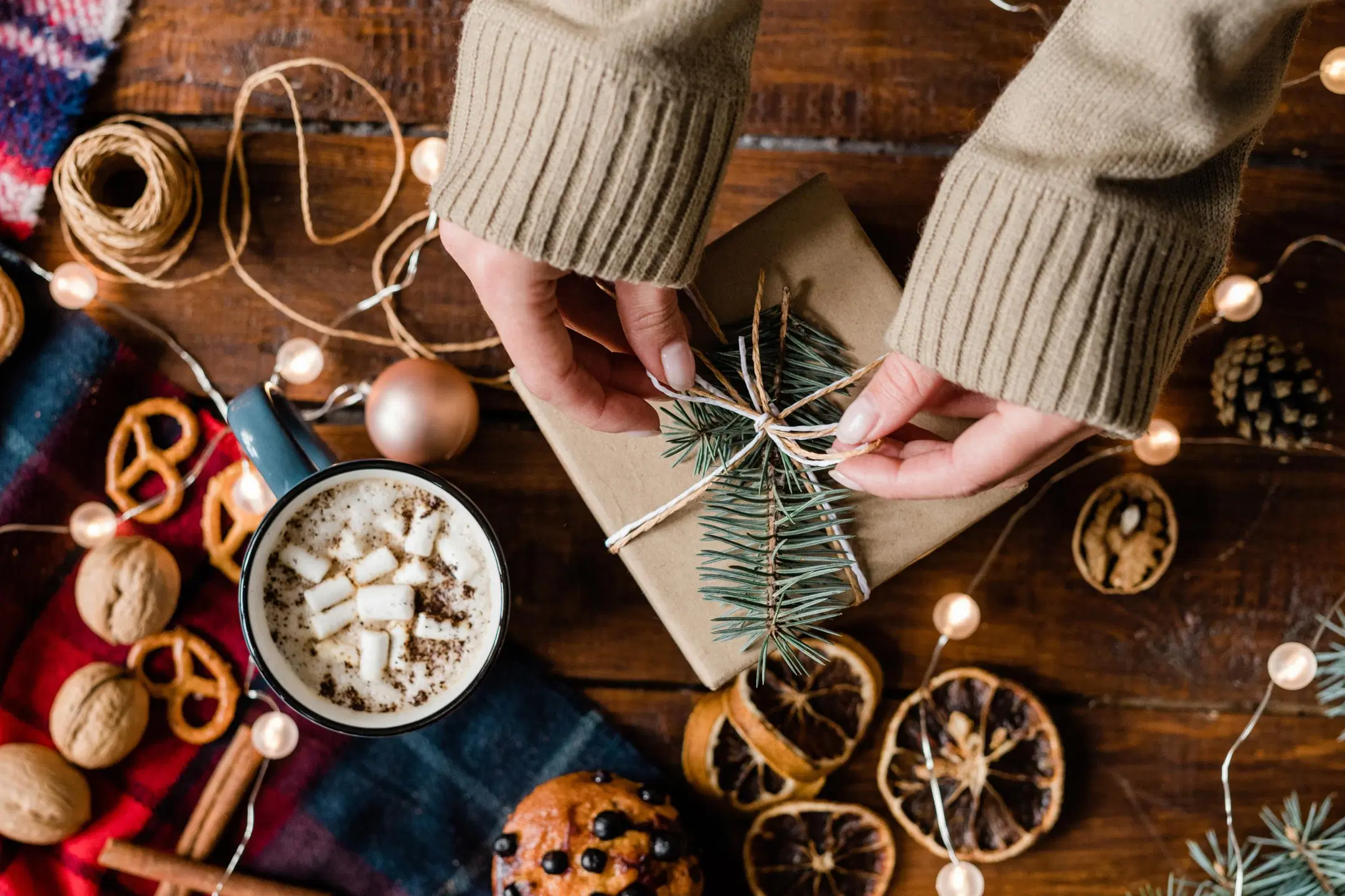 Itse tehtyn lahjan paketointi, ympärillä kuivattuja appelsiineja, jouluvalot ja herkkuja