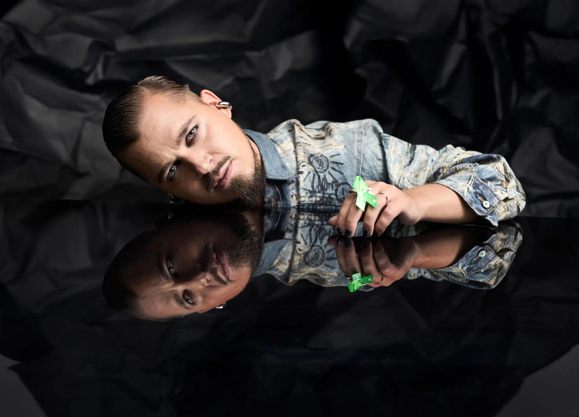 Jere Pöyhönen nojaa peilaavaa mustaa pöytää vasten Mielinauha kädessään ja katsoo kameraan.