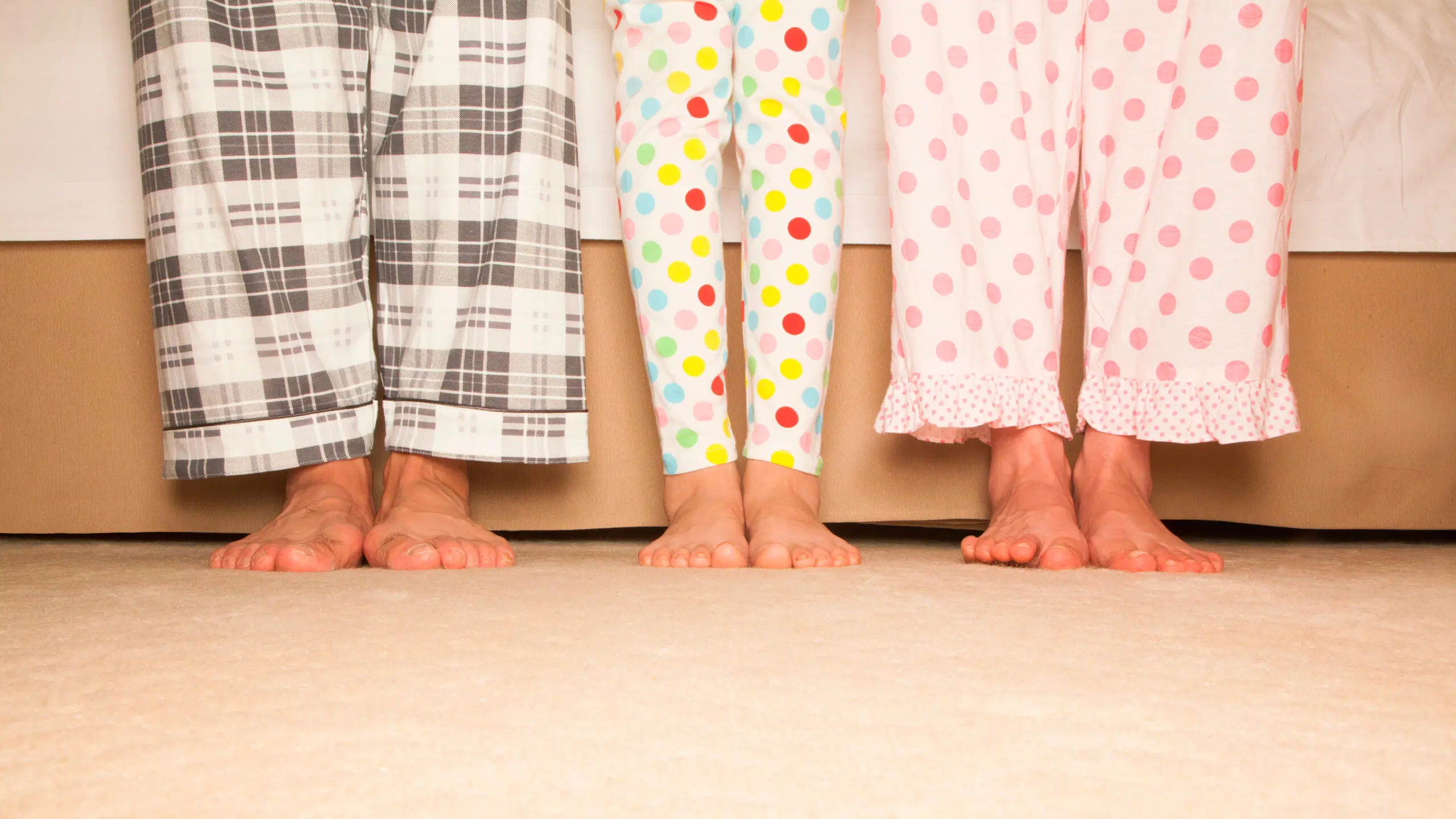 Miehen, lapsen ja naisen jalat rivissä. Kaikilla on pyjamahousut.
