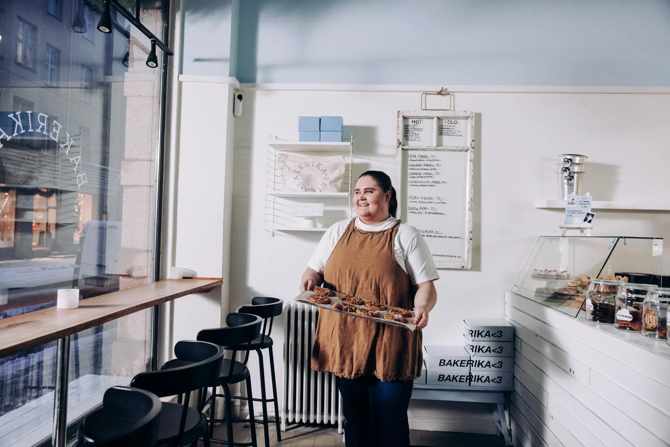 Erika Poussa seisoo kahvilassa pellillinen keksejä käsissään.