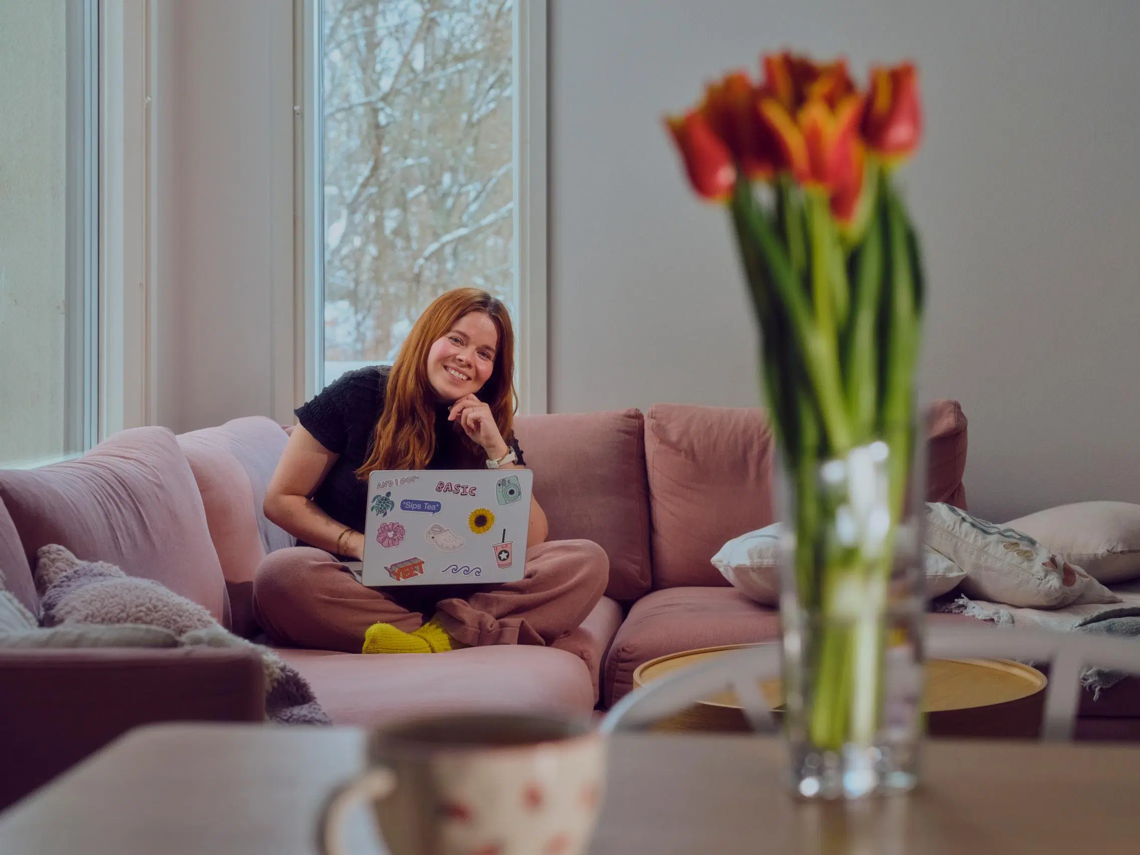 Salla Salmela istuu vaaleanpunaisella sohvalla kannettava tietokone sylissään.