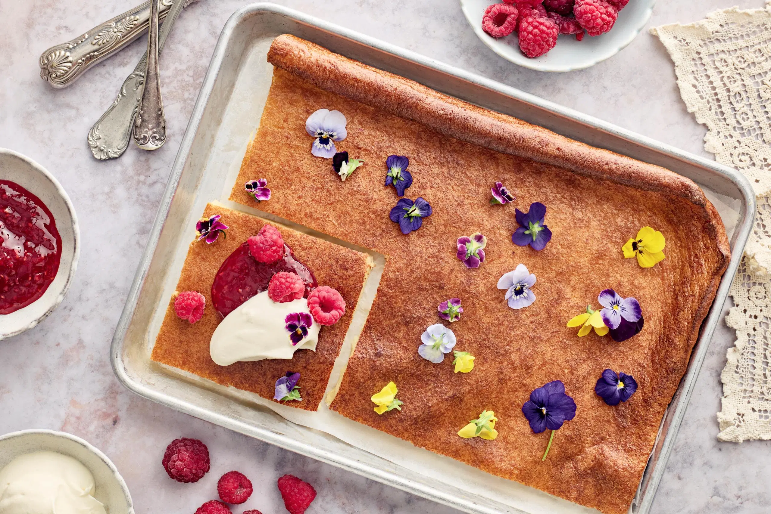 Pannukakku, joka on koristeltu syötävillä kukilla ja viimeistelty hillolla ja vadelmilla. 