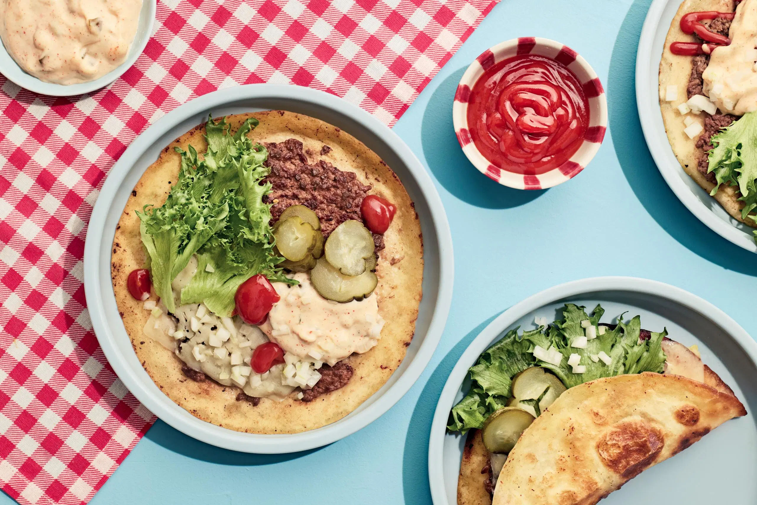 Lautasella burgeritaco, jossa täytteenä jauhelihaa, salaattia, suolakurkkua ja hampurilaiskastiketta.