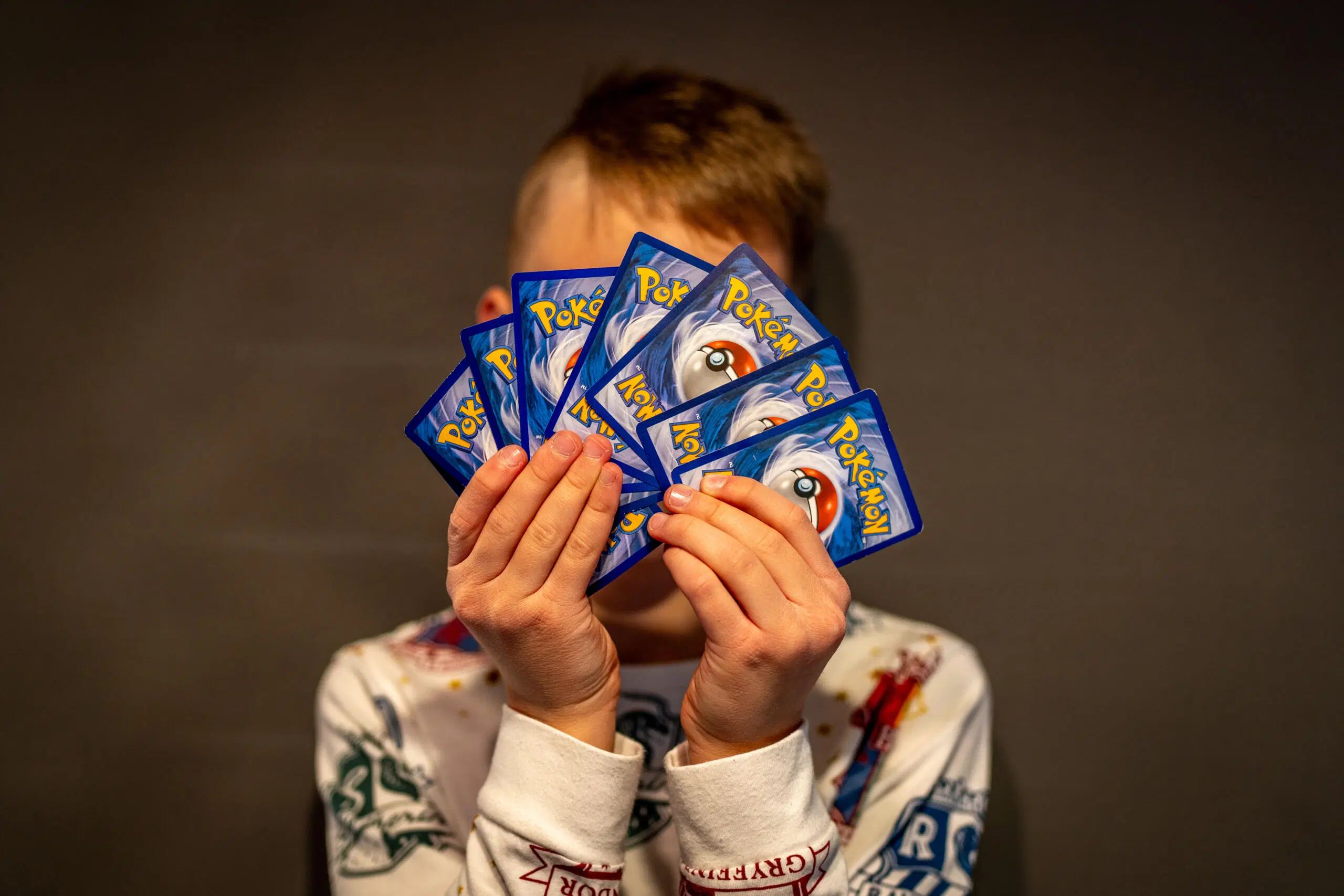 Lapsi pitelee käsissään Pokemon-kortteja ja peittää korteilla kasvonsa