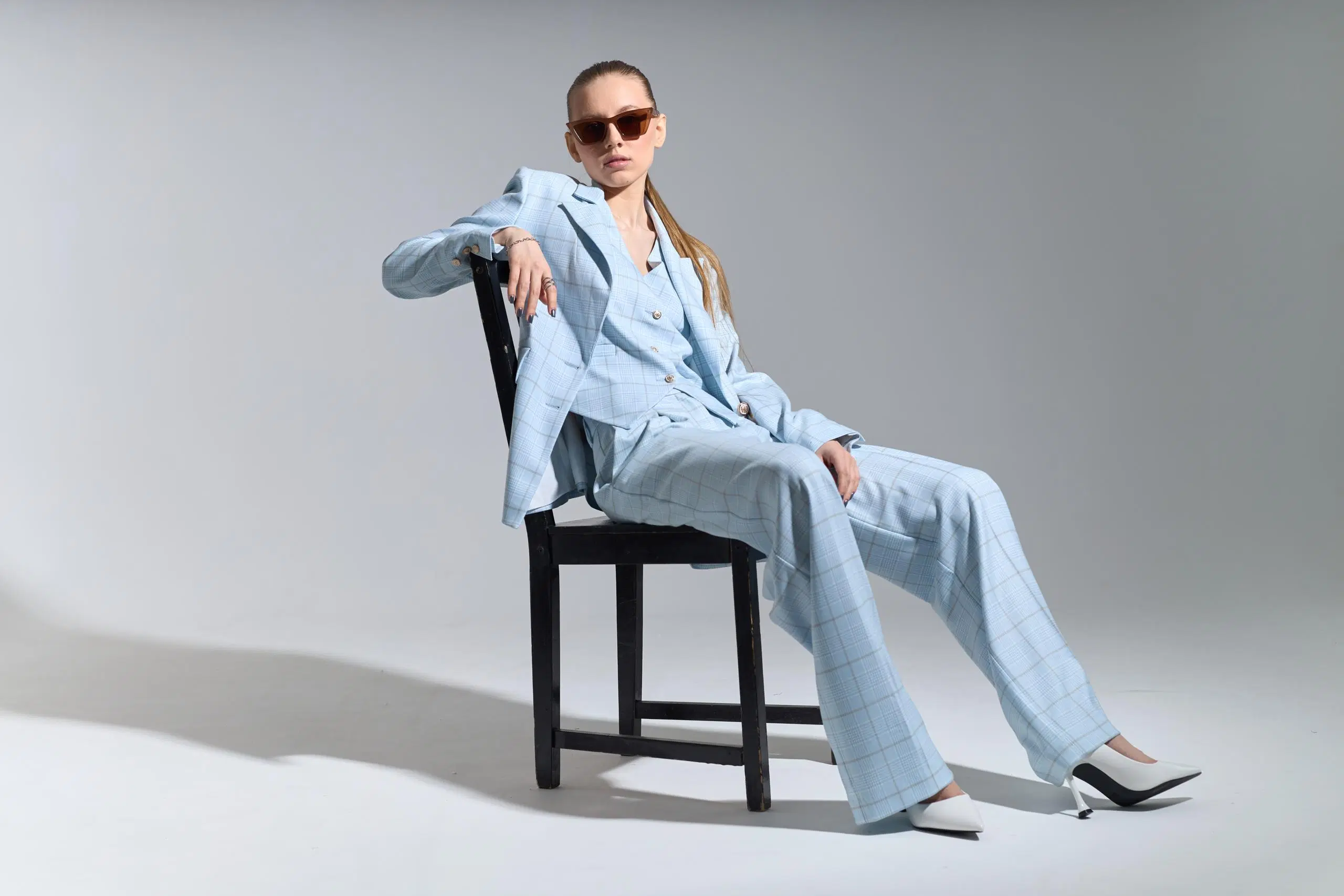 Vaaleansiniseen housupukuun pukeutunut nainen istuu tuolilla rennosti aurinkolasit päässään