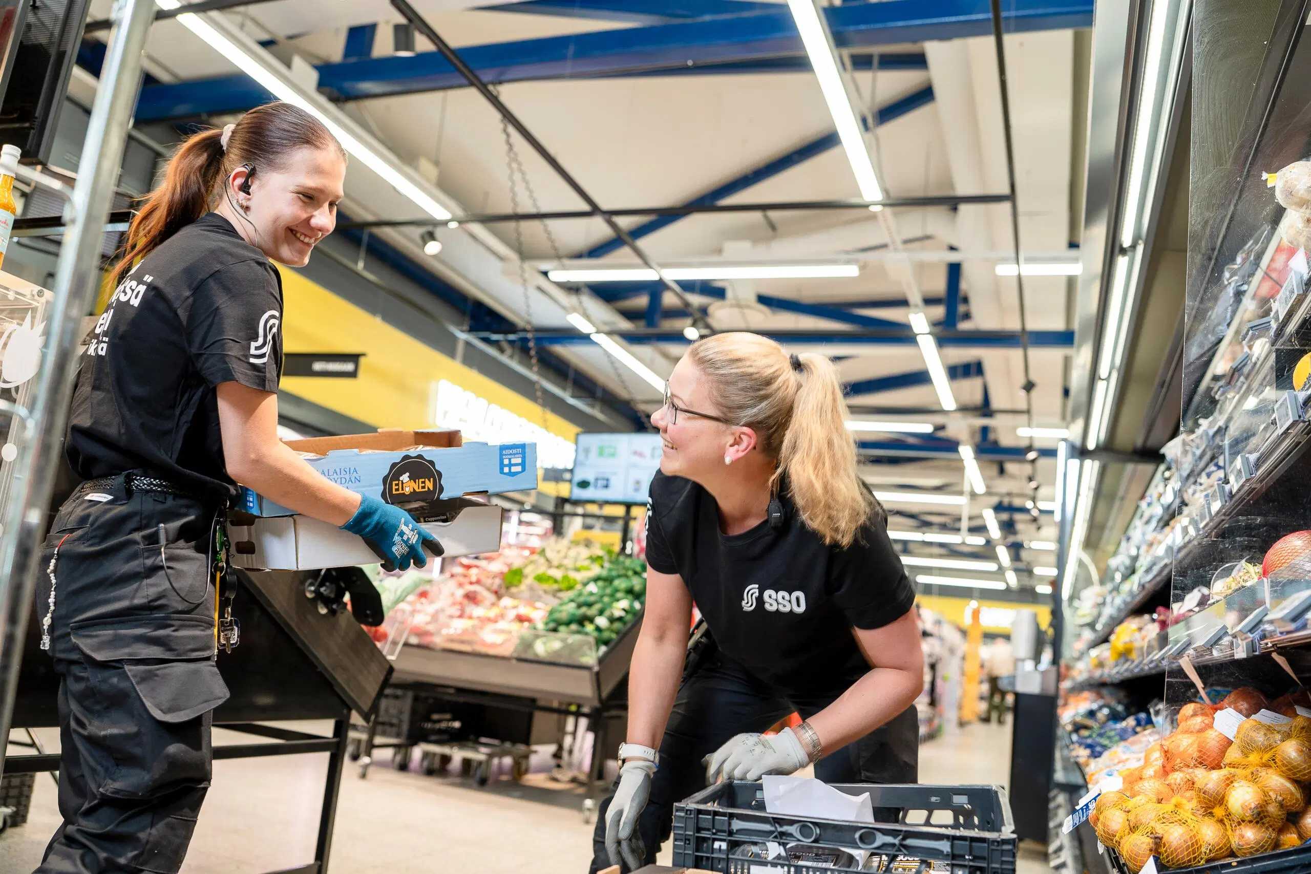Kaksi iloista naista purkaa kuormaa kaupassa.