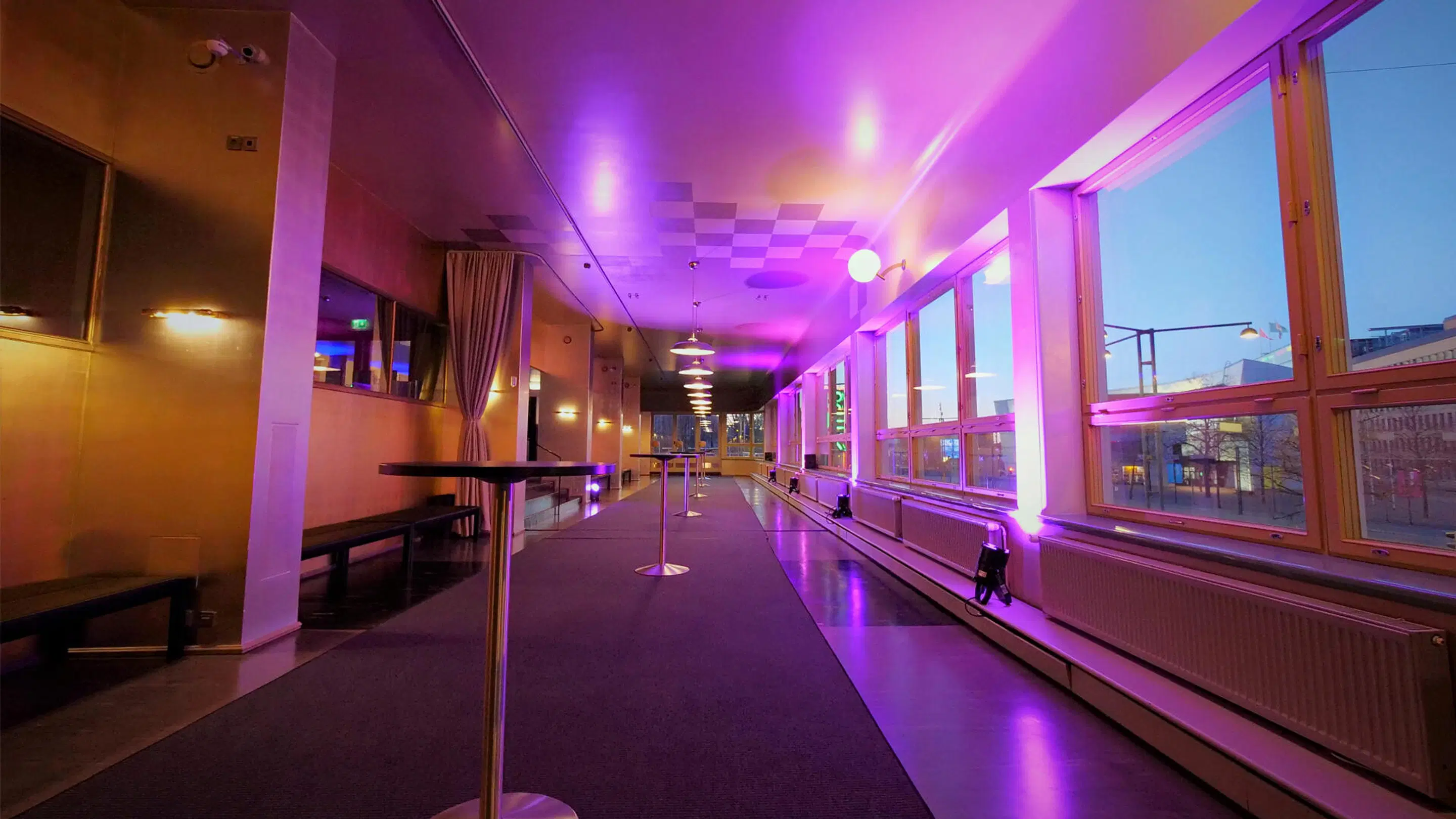 Long hallway with purple lighting. Benches along left wall, large windows on right. Dark carpeted floor.