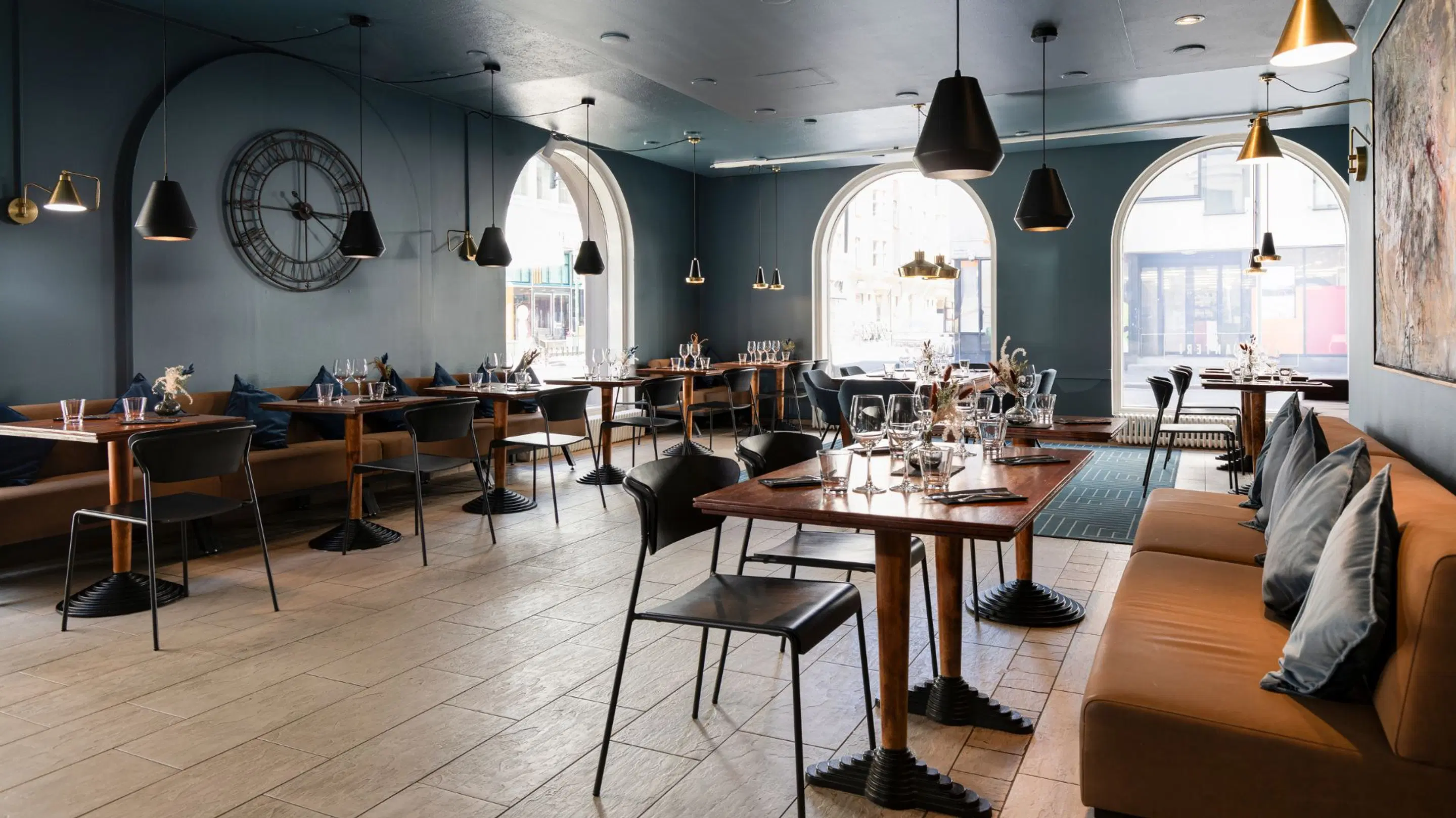 Stylishly decorated restaurant with teal walls, wooden flooring and large arched windows. Wooden tables with black chairs and bench seating.