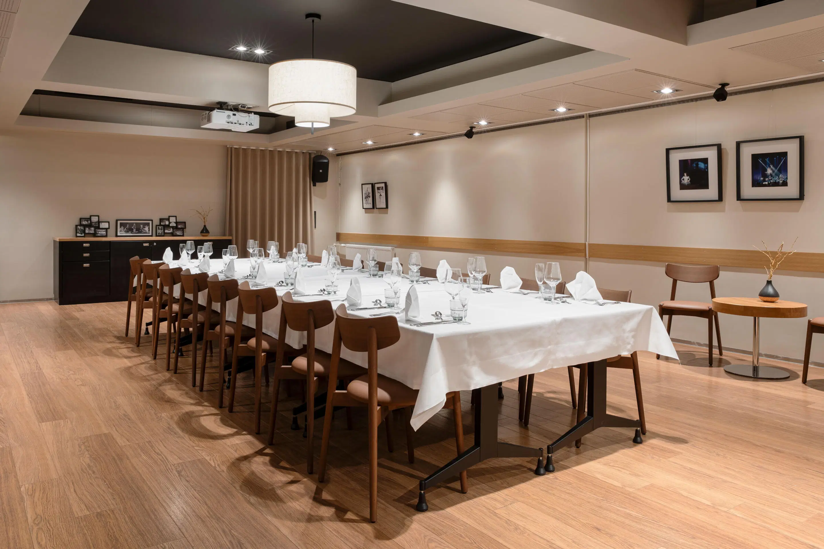 Elegant private dining room with long table covered in white tablecloth and place settings. Wooden floor and warm lighting.