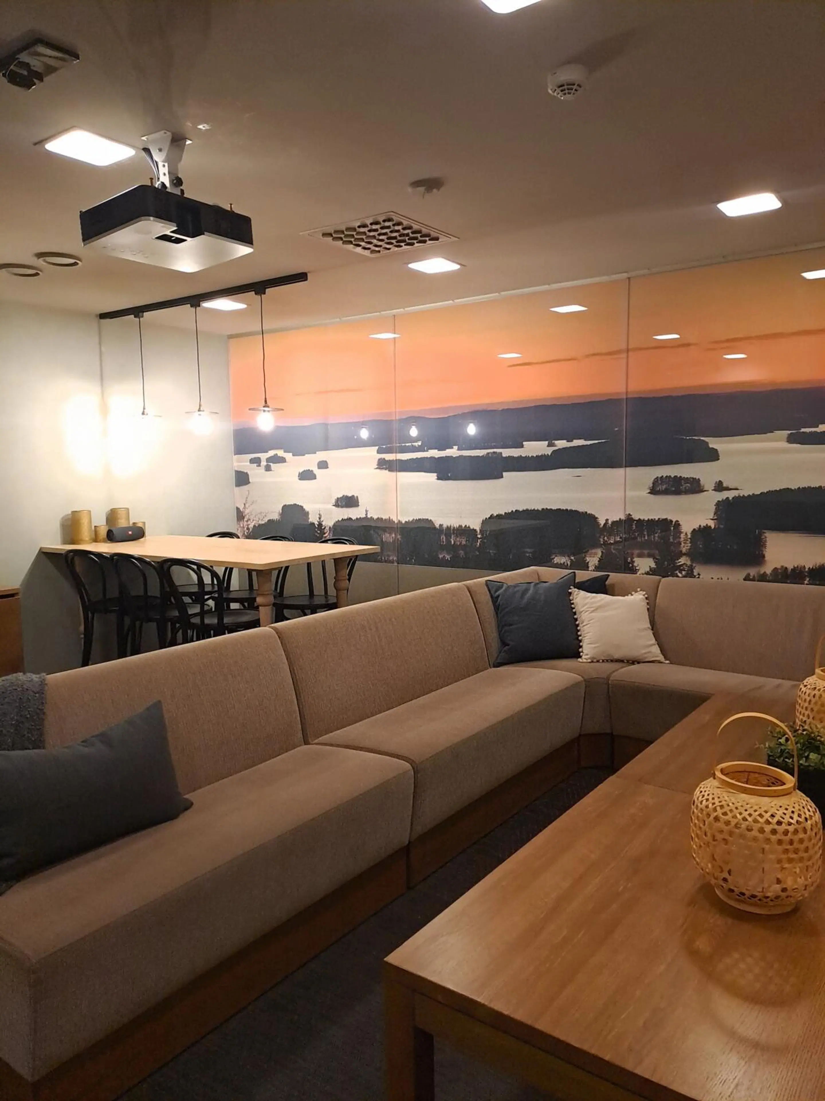 Modernt loungeområde med en beige hörnsoffa, träbord och en stor landskapsbild av en sjövy vid solnedgången. Rummet har även ett matbord.