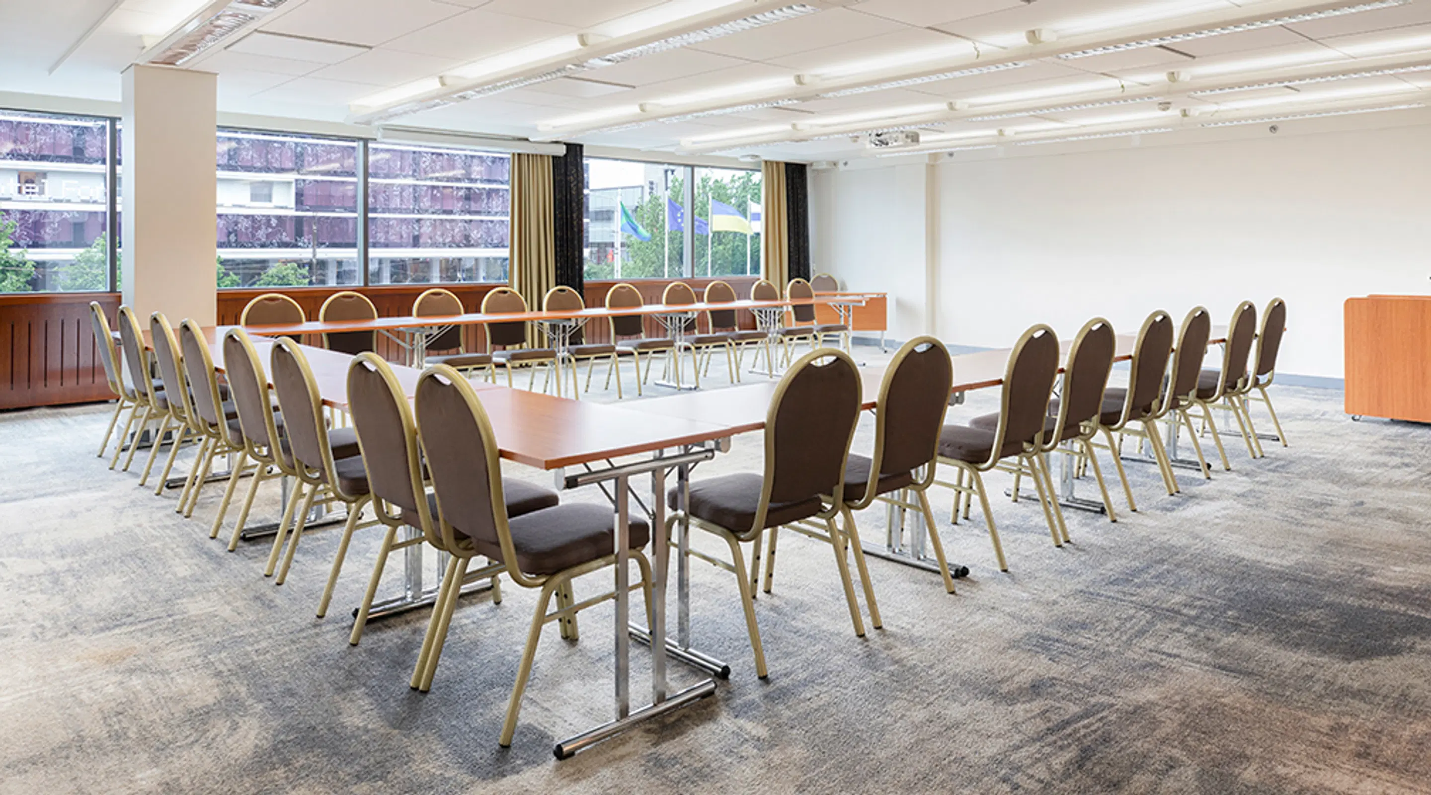 Bright conference room with long tables and upholstered chairs in rows. Space has level access, but floor has low-pile carpeting.