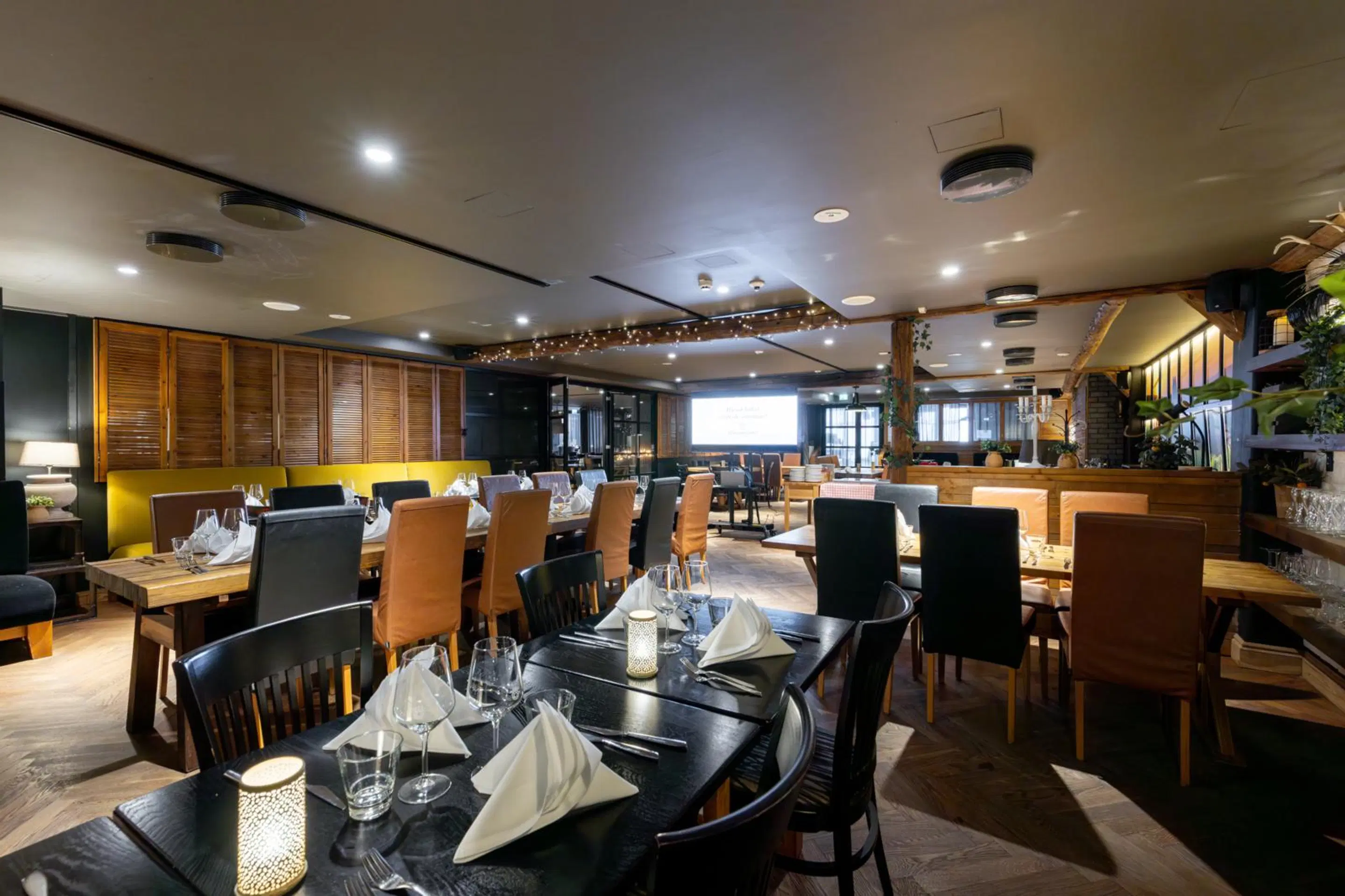 Stilfullt inredd restaurang med trägolv och både svarta och bruna stolar. Rymlig matsal med vita servetter och vinglas på borden.