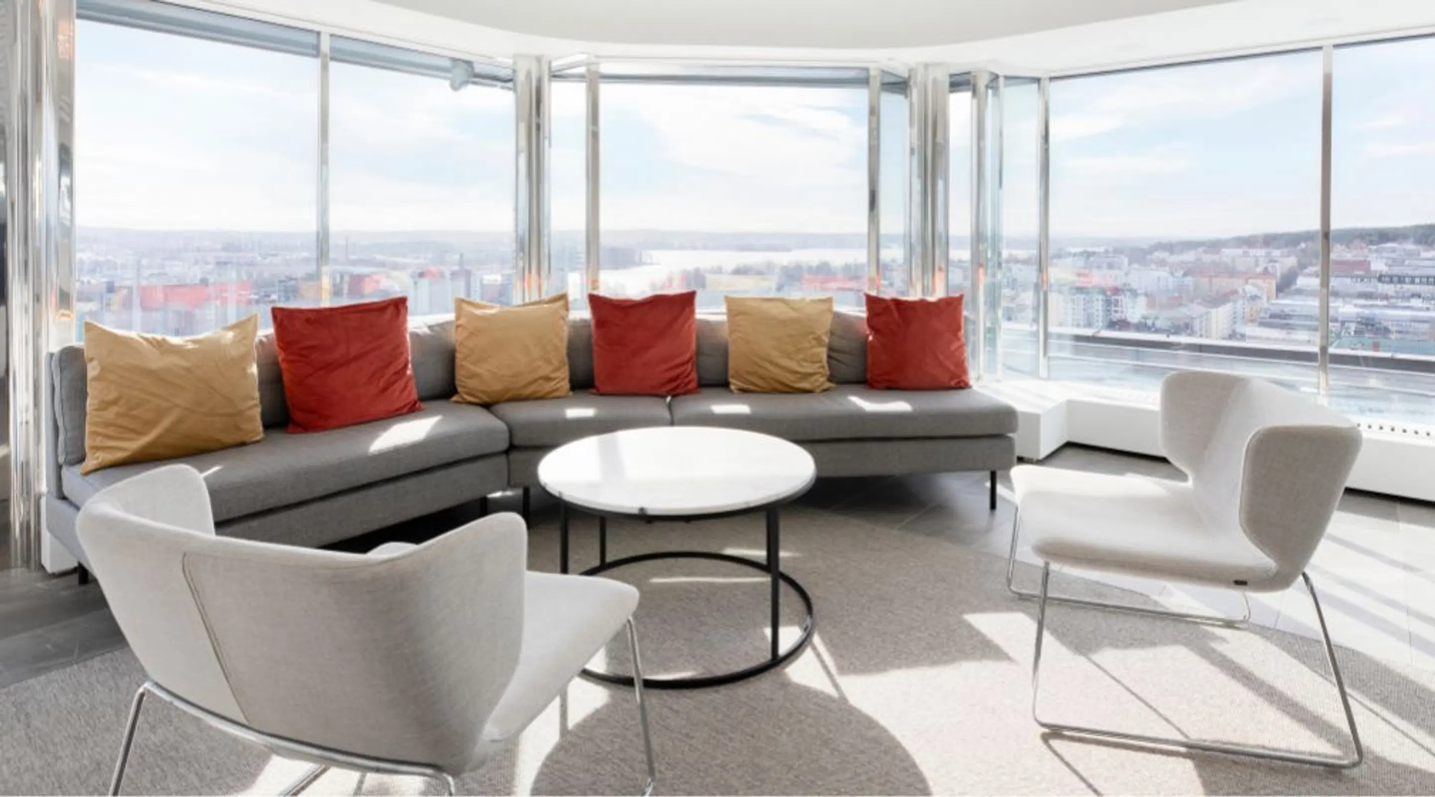Modern high-rise lounge area with curved sofas and chairs, panoramic windows with city views.