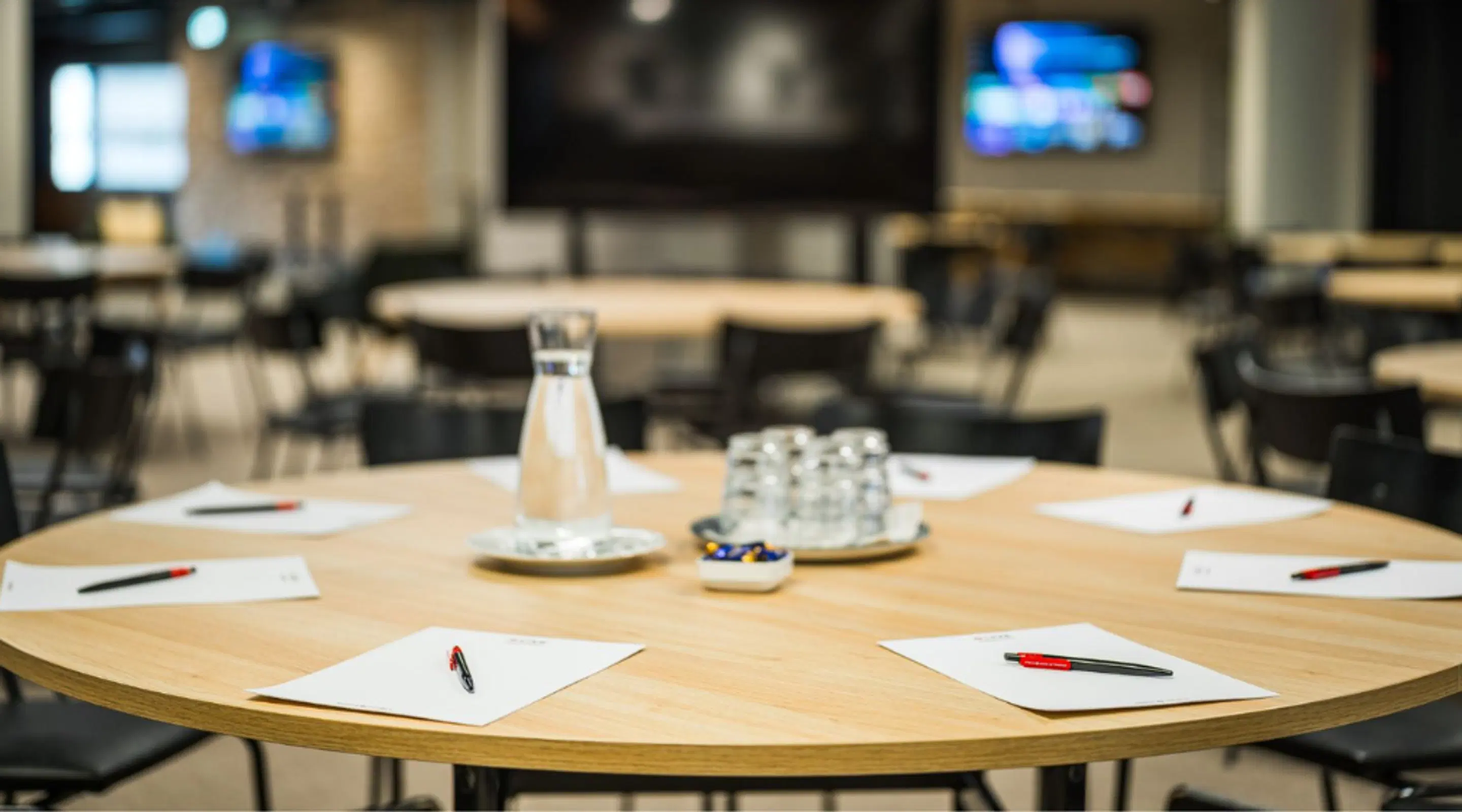 Round meeting table prepared, with carafe and glasses in the center, surrounded by chairs.