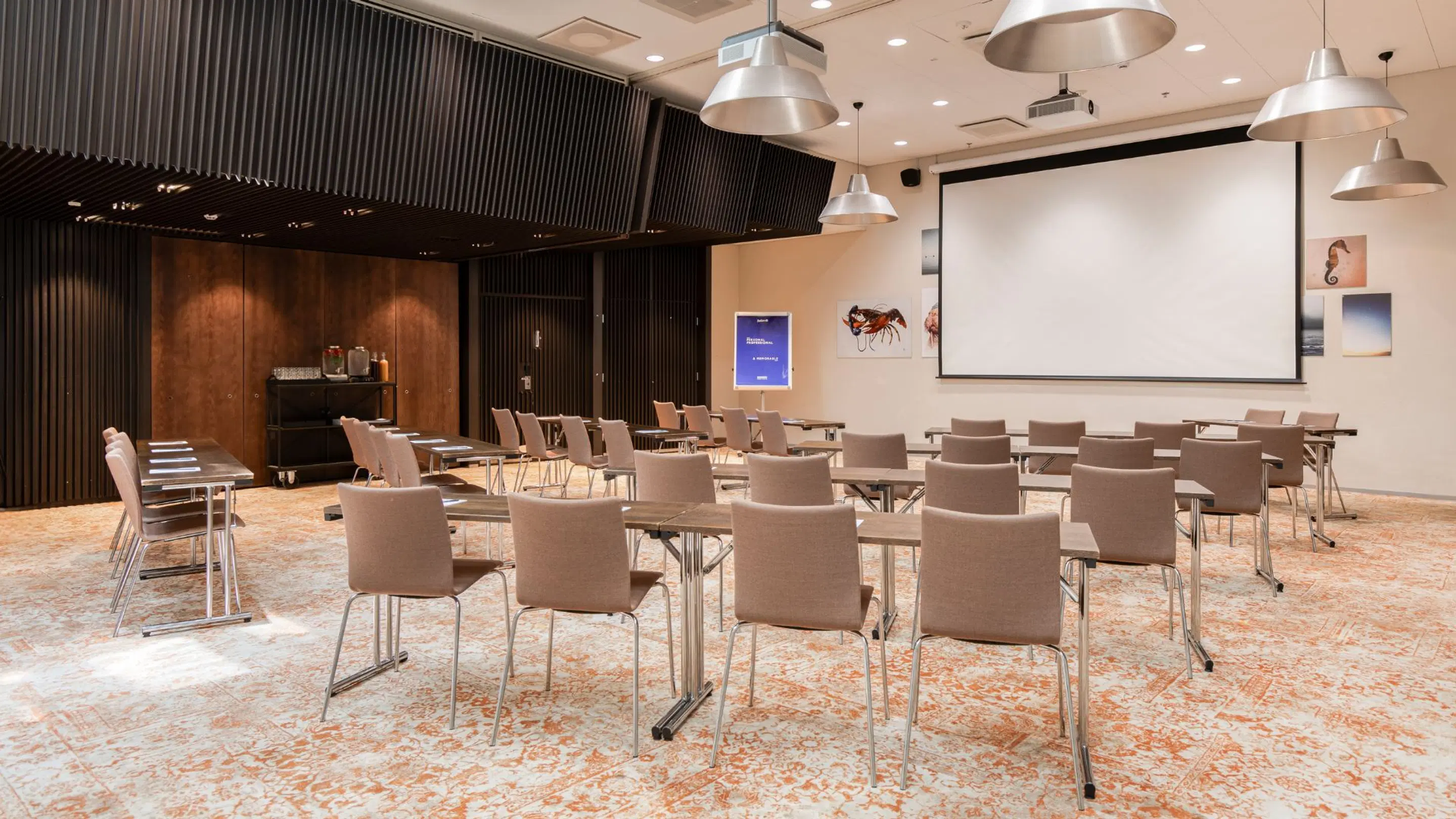 Modern meeting room with table arrangements, projection screen and dark wood paneling. Level floor and well-lit space.