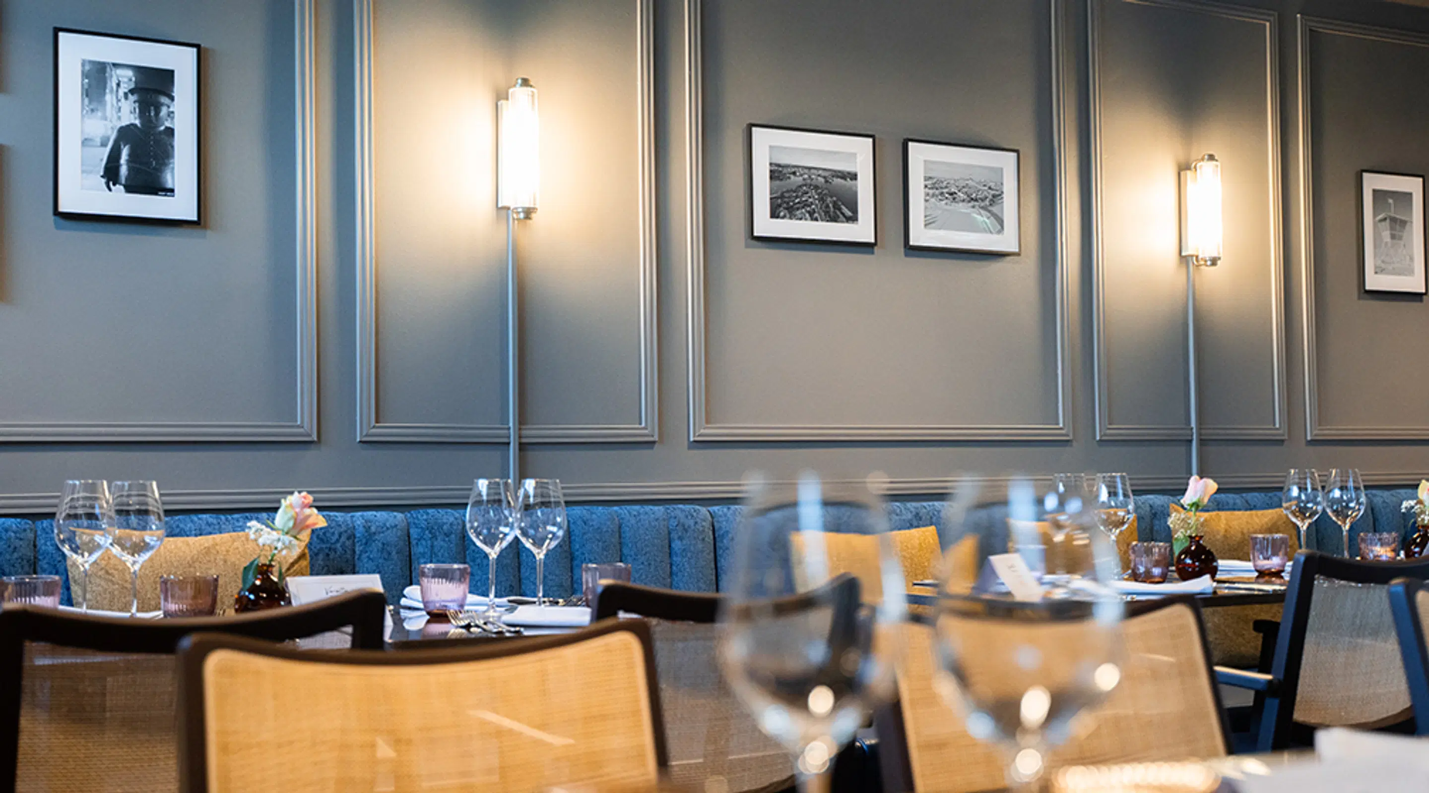 Restaurant interior with blue banquette seating, set tables and light grey walls framed by white moulding.