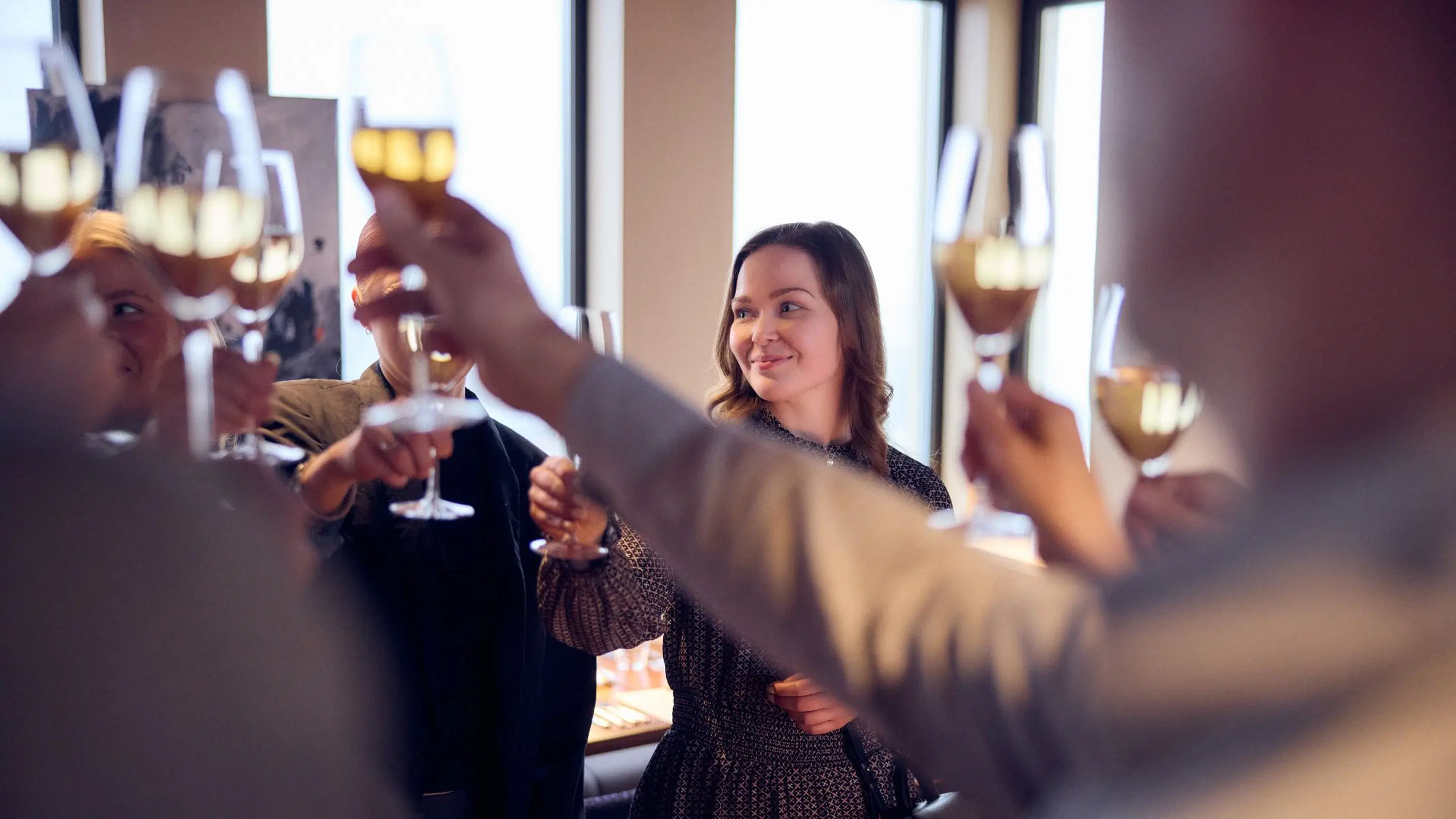 Personer skålar med champagneglas vid en festlig tillställning i ett ljust utrymme med stora fönster.