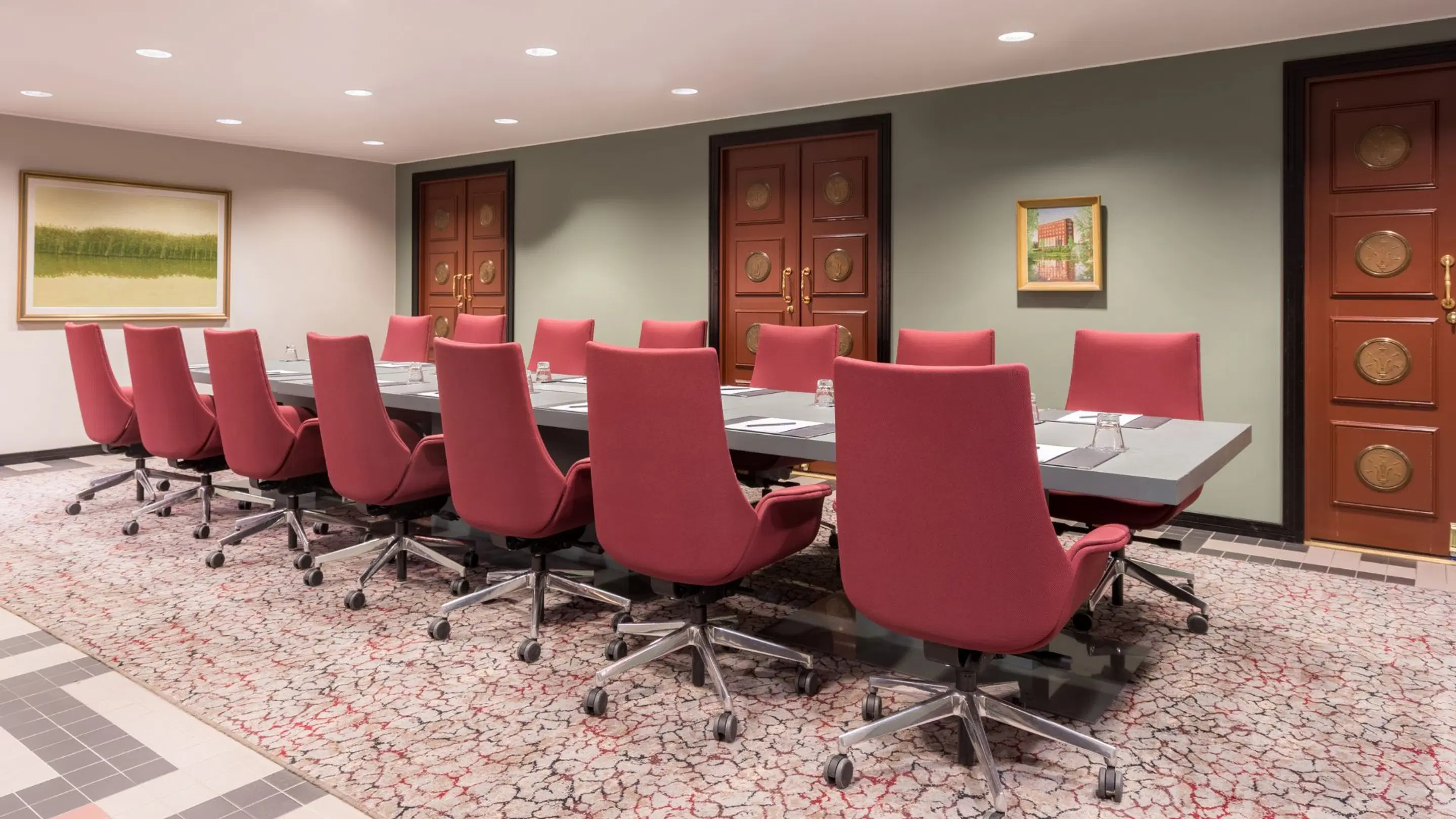 Conference room with red rolling chairs around long table. Room features patterned carpet and decorative wooden doors.