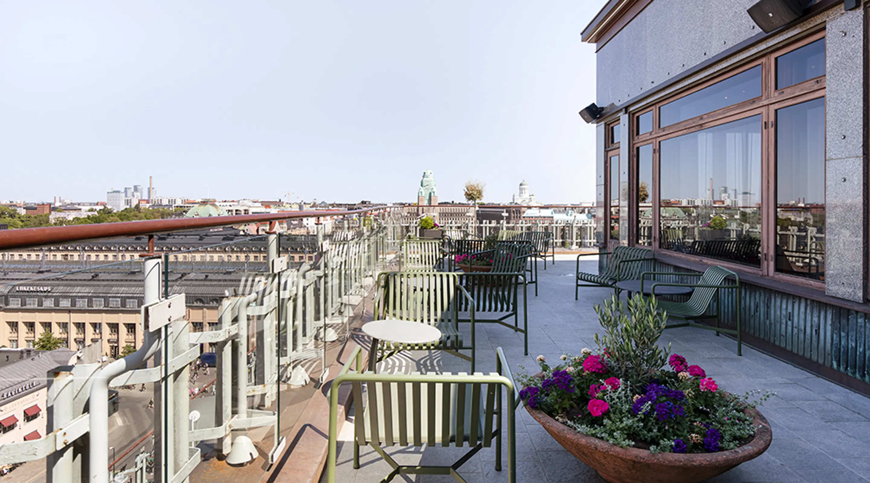 Takterrass med sittgrupper med randiga stolar och runda bord. Blomkruka med färgglada blommor.