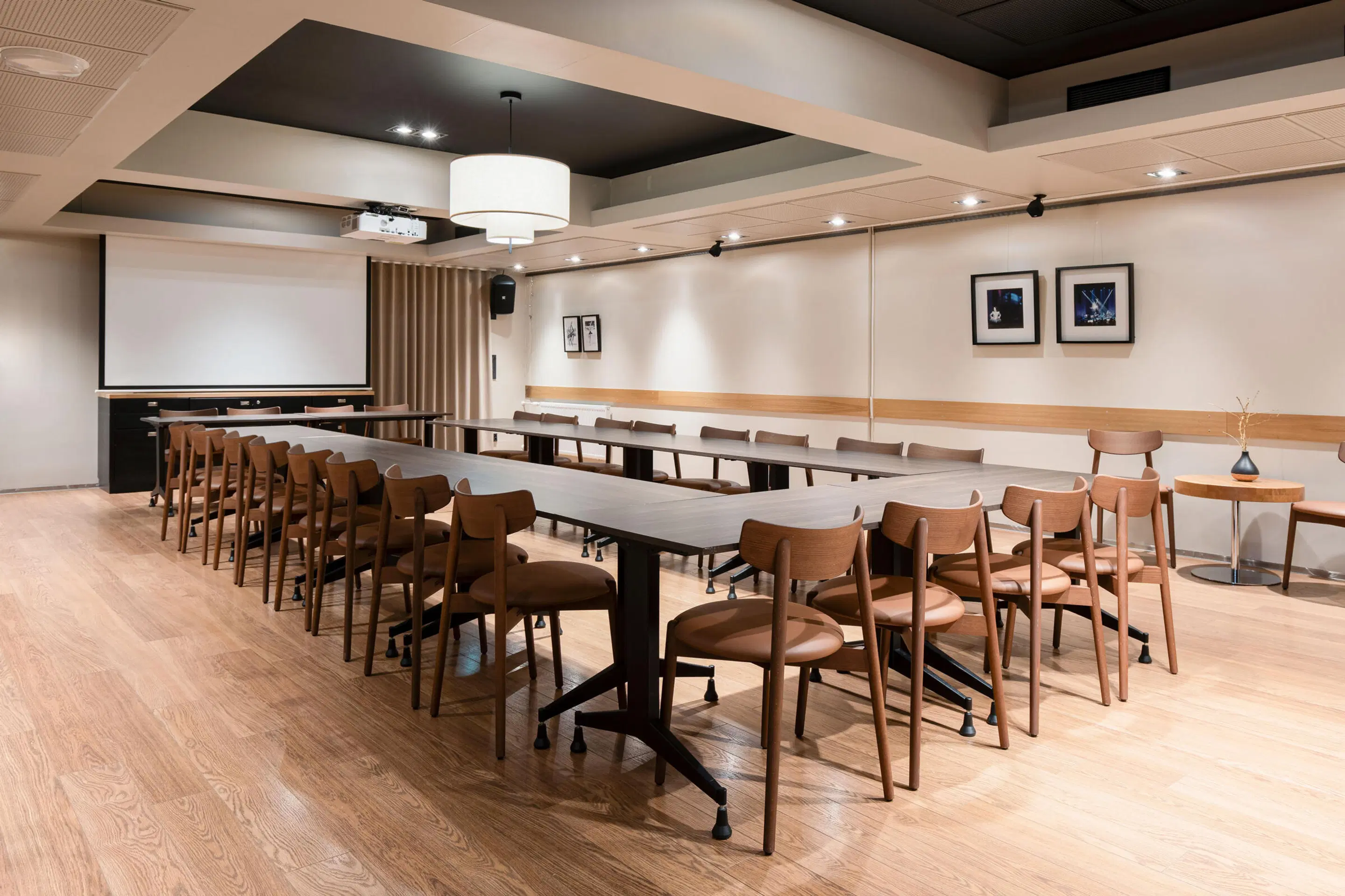 Modern conference room with a long table, wooden chairs and a projection screen. Light wooden floor and even lighting.